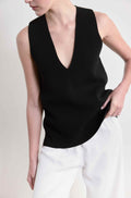 Person wearing a black sleeveless top and white pants on a plain background