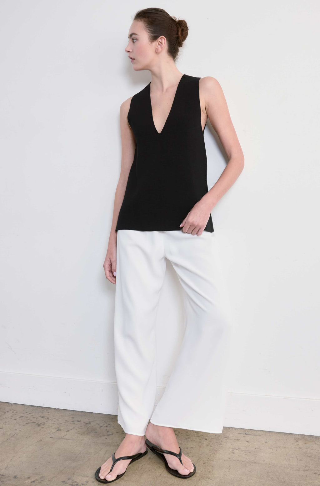 Woman wearing a black sleeveless top and white pants against a plain background
