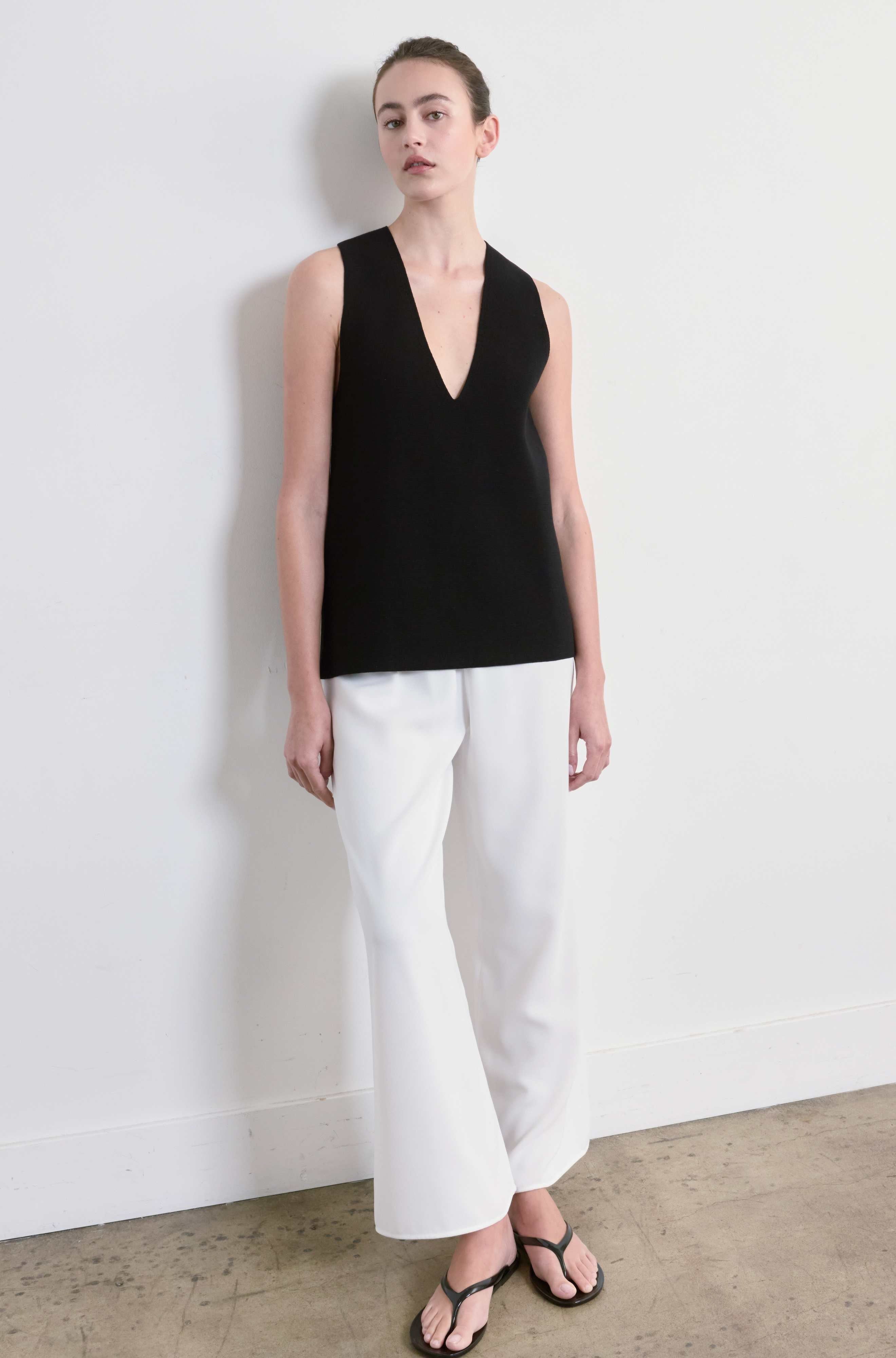 Person wearing a black sleeveless top and white pants against a plain background