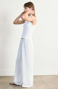 Woman wearing a white tank top and wide-leg pants against a plain background