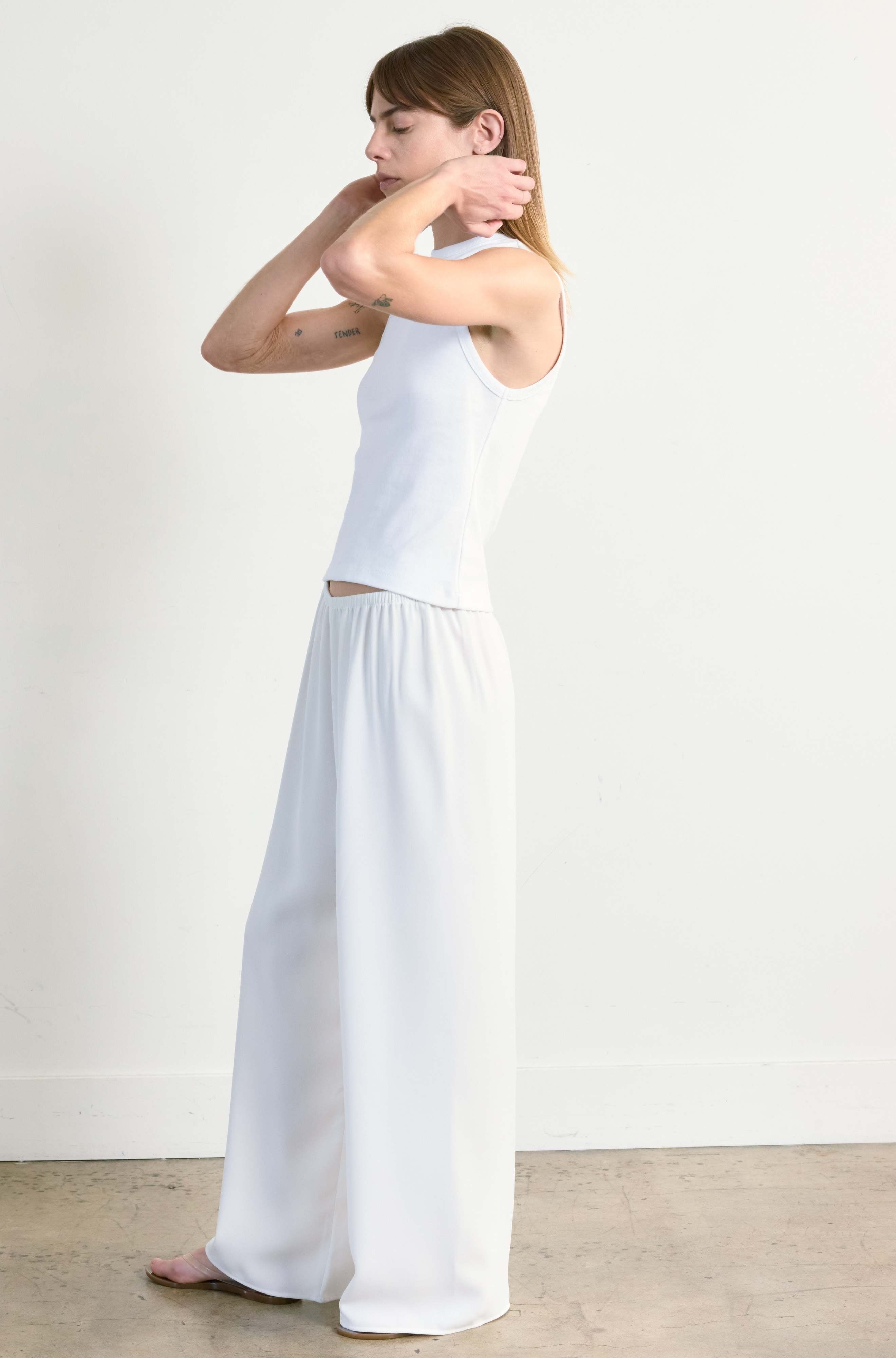 Woman wearing a white tank top and wide-leg pants against a plain background