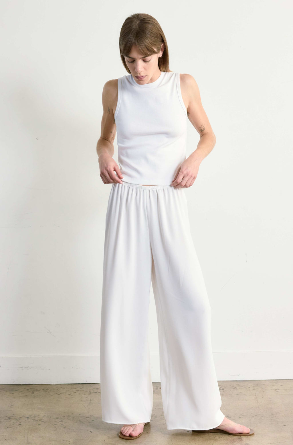Woman wearing a white sleeveless top and wide-leg pants against a plain background