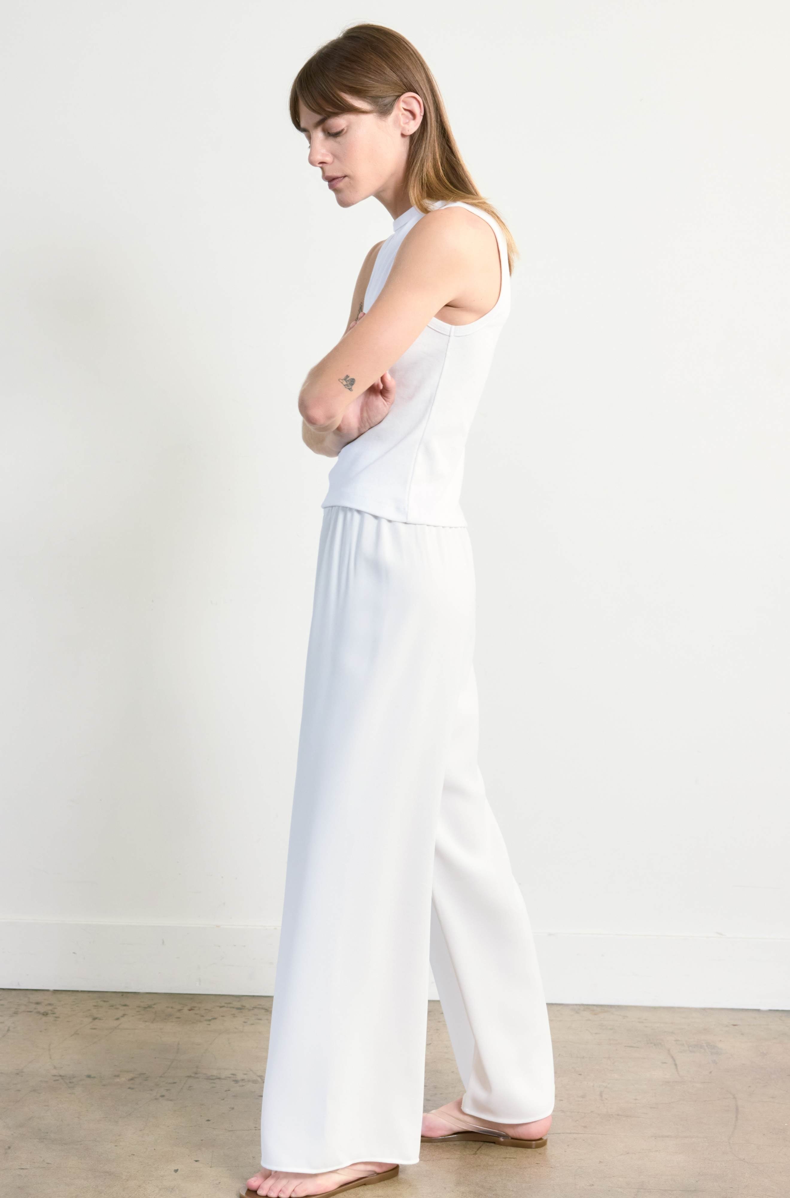 Woman wearing a white sleeveless top and wide-leg pants against a plain background