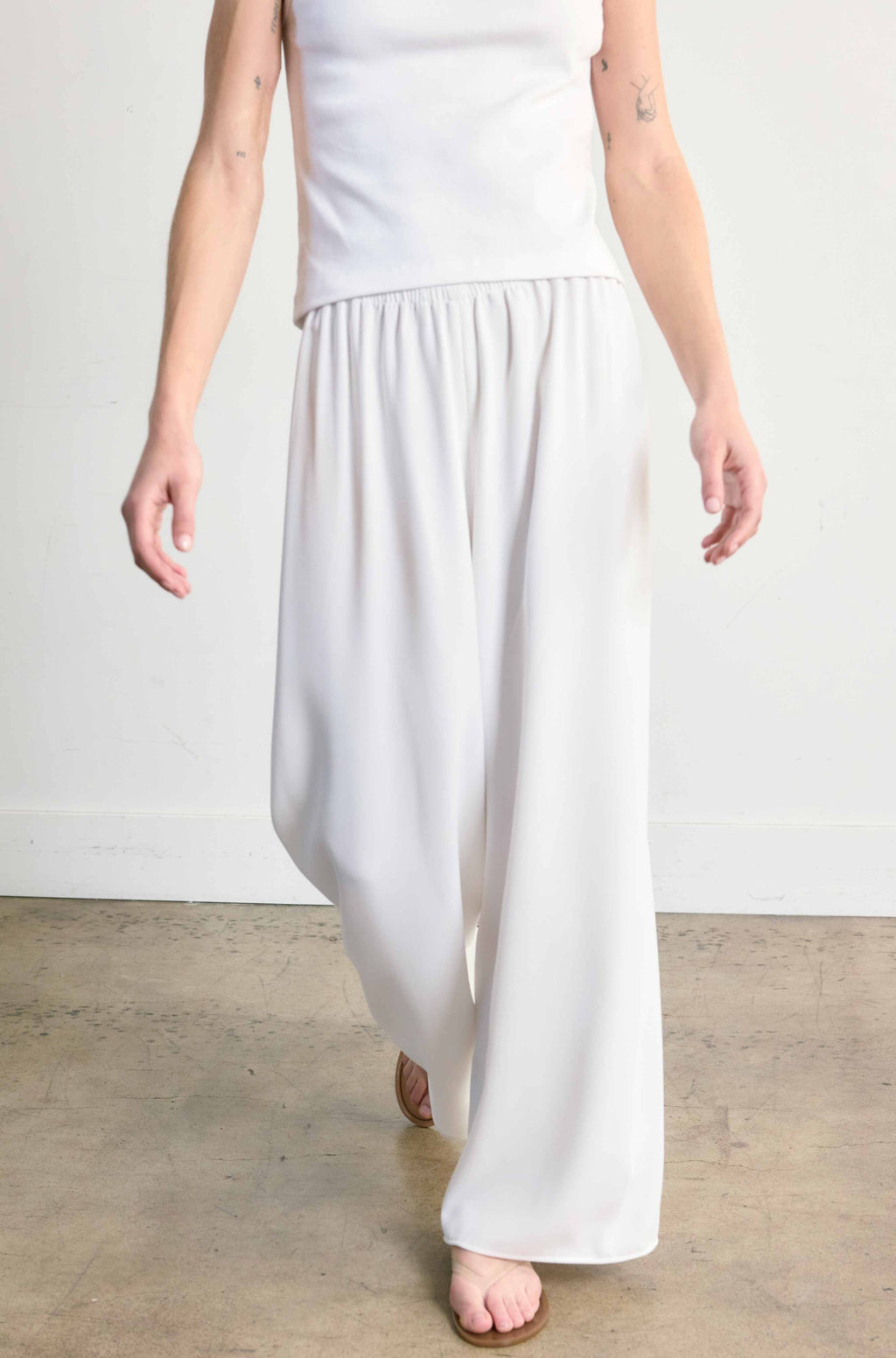 Person wearing a white top and wide-leg pants on a plain background