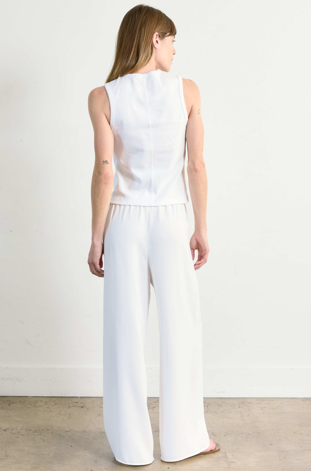 Woman wearing a white sleeveless top and wide-leg pants against a plain background