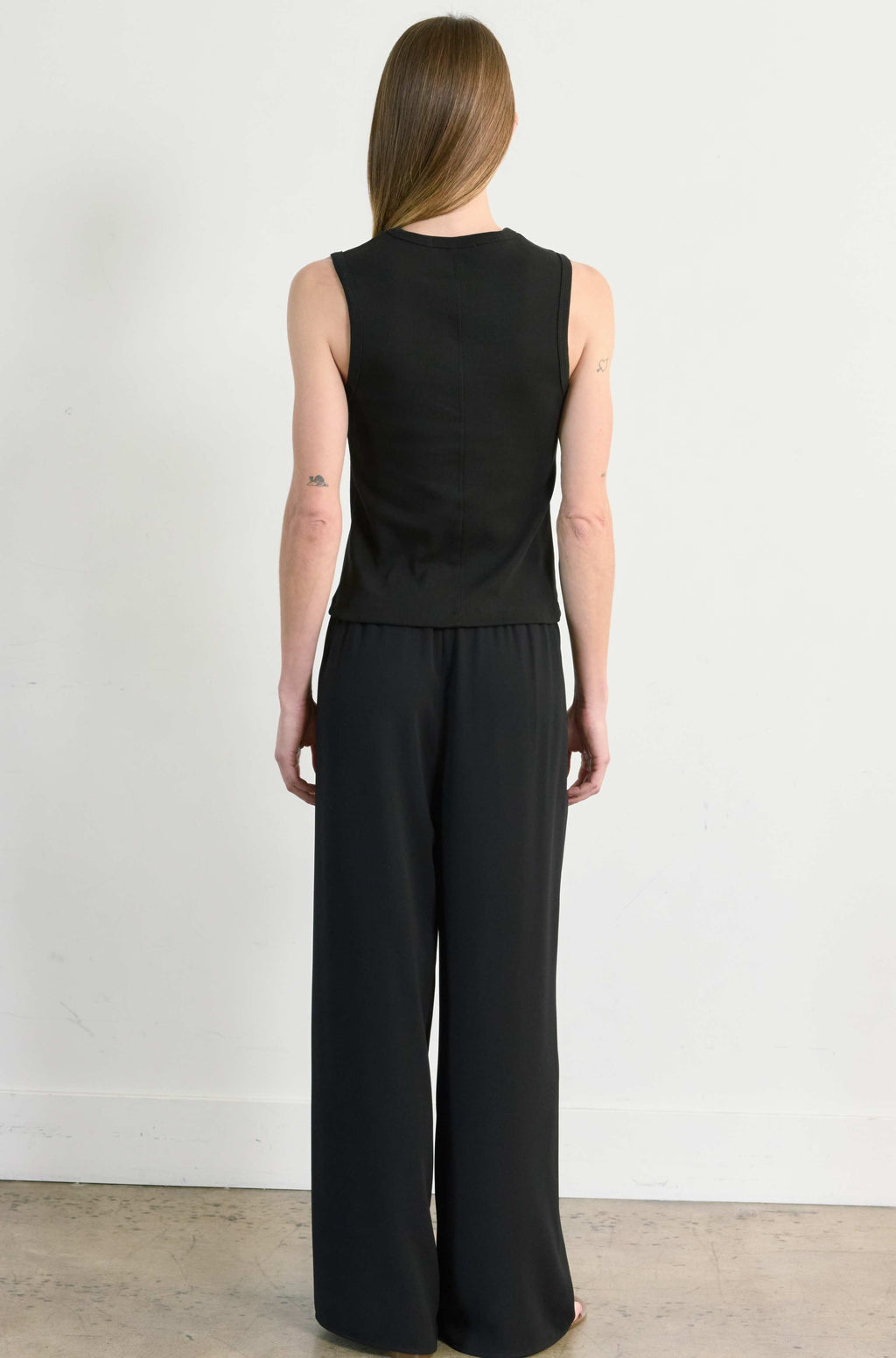 Person wearing a black sleeveless top and wide-leg pants against a white background