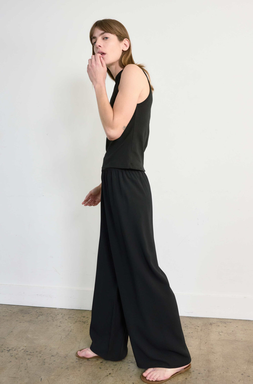 Woman wearing a black sleeveless top and wide-leg pants against a white wall.