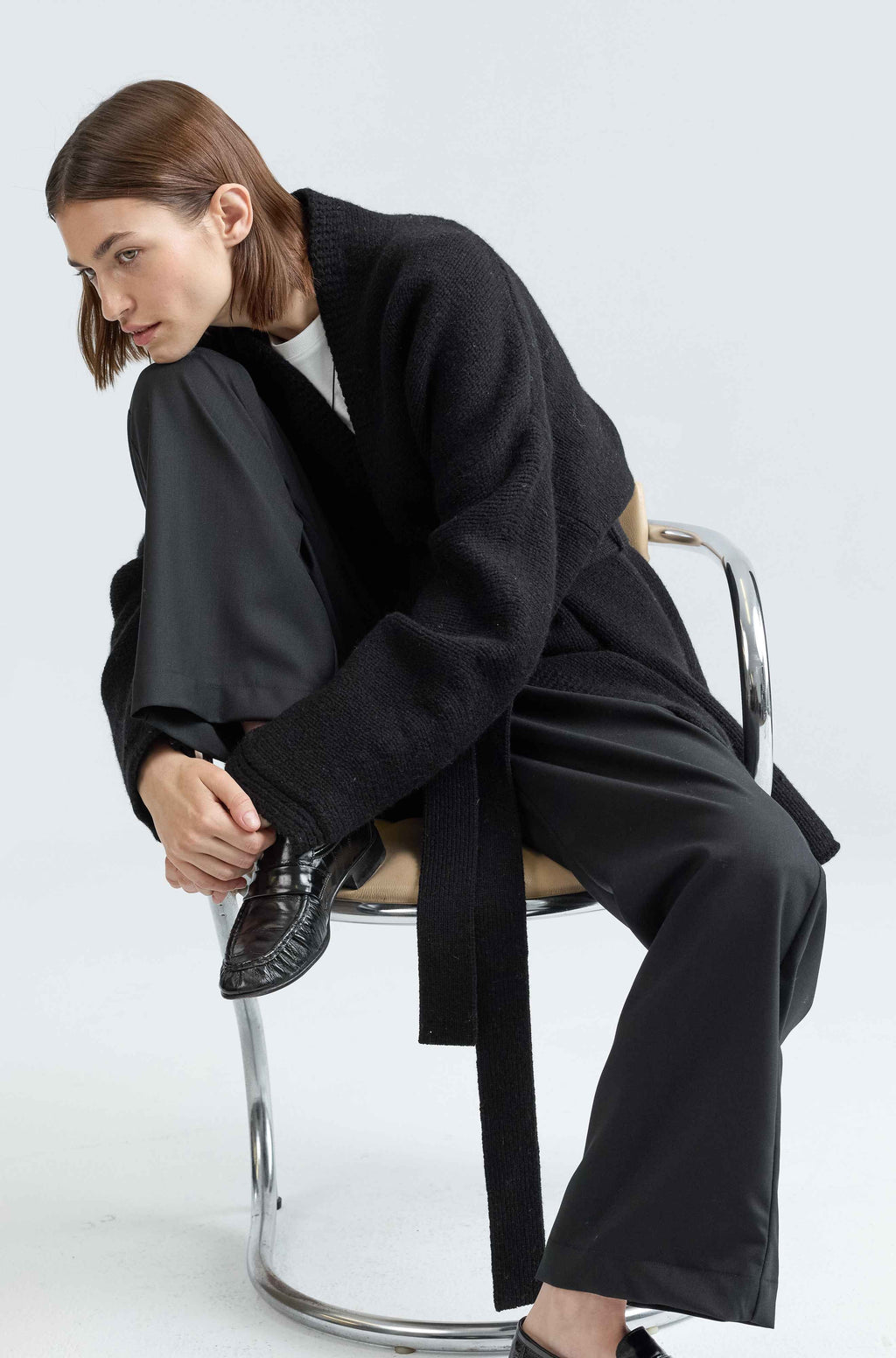 Person wearing a black wool wrap sweater sitting on a chair against a white background