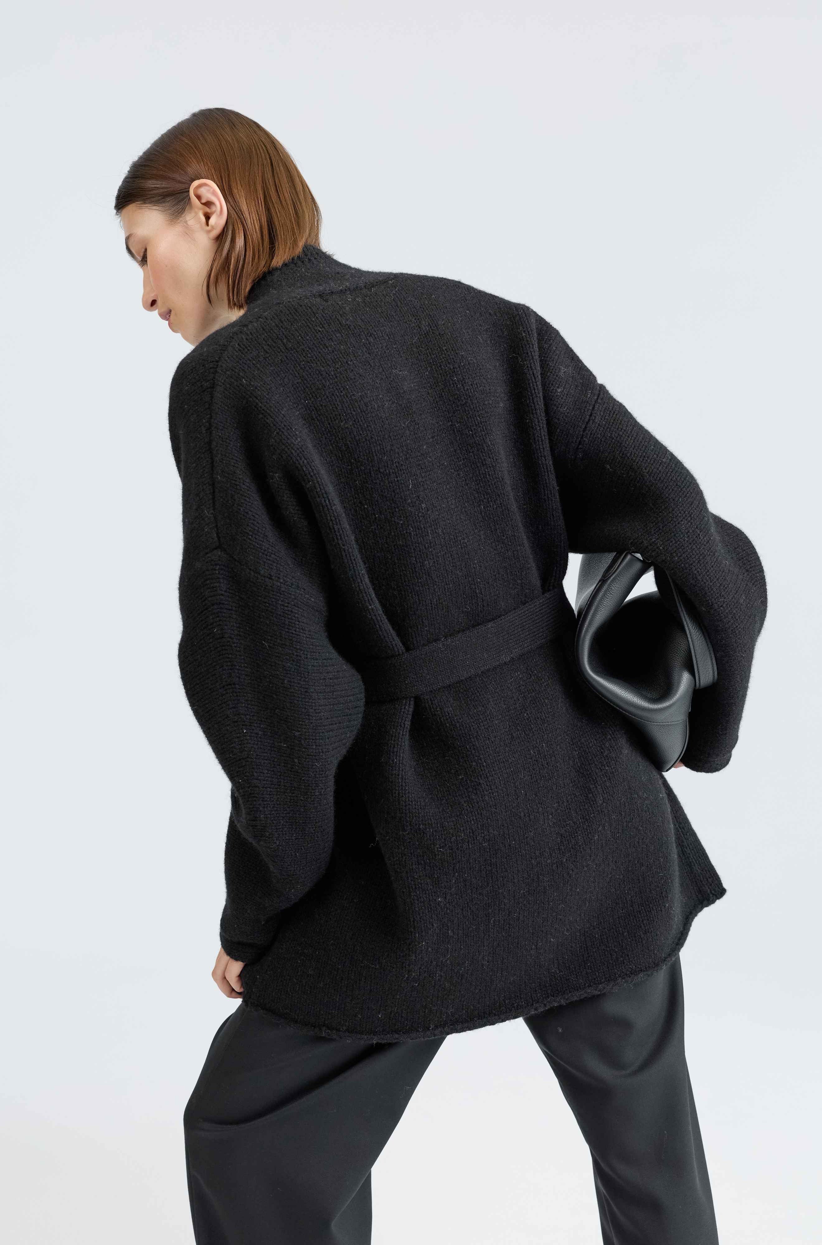 Person wearing a black coat with a belt on a white background