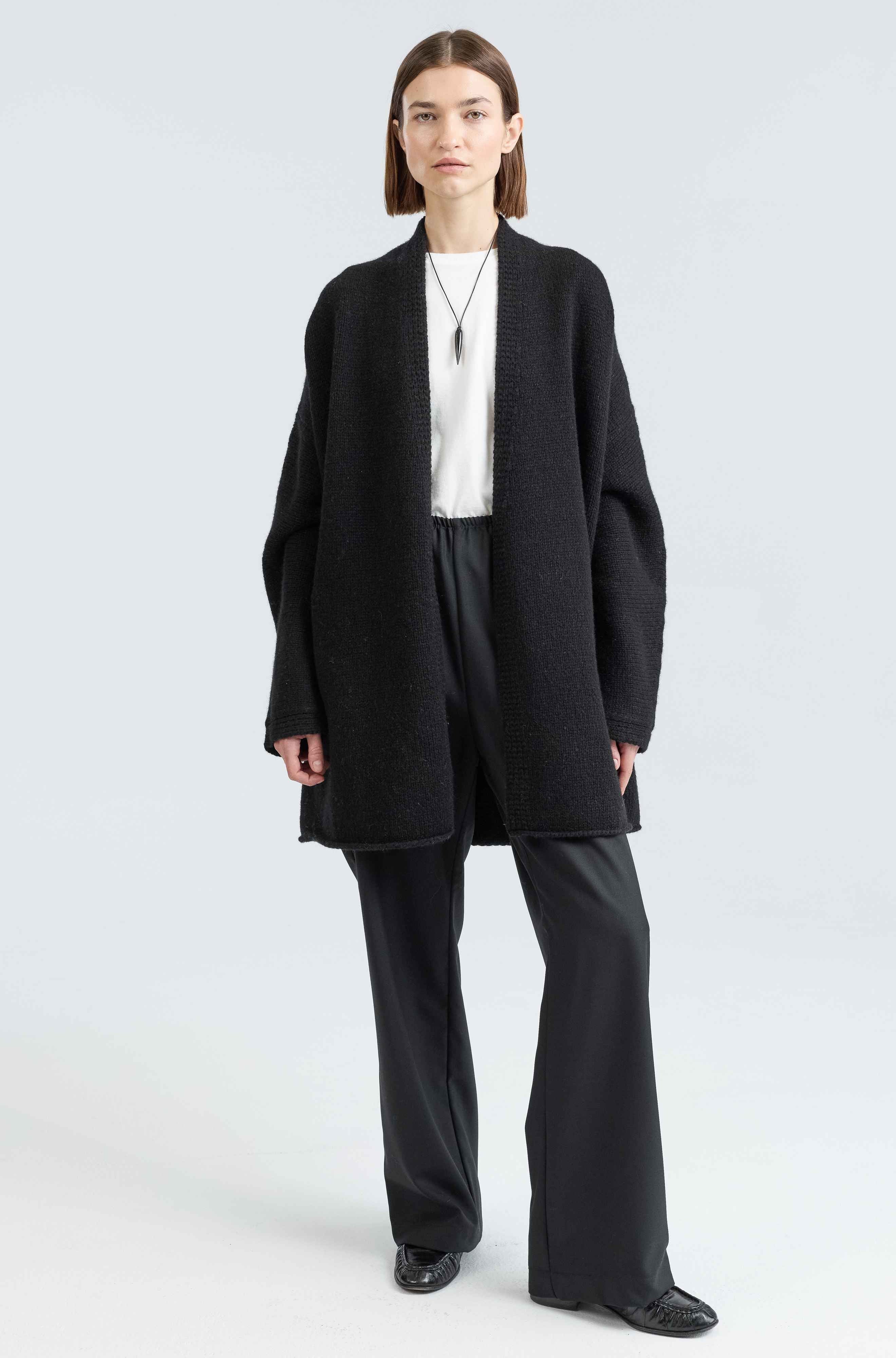 Person wearing a black coat, white shirt, and black pants on a light gray background