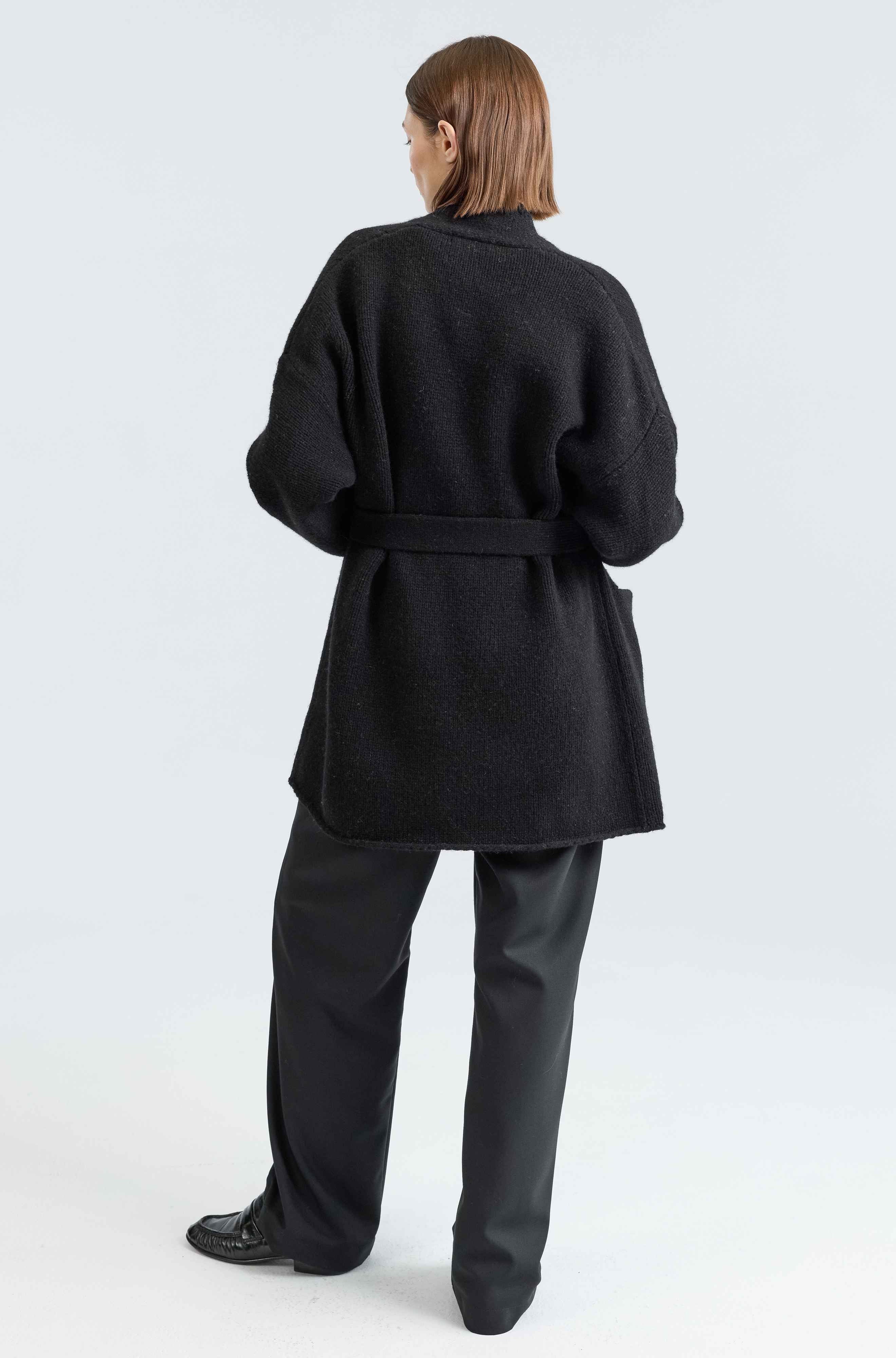 Person wearing a black coat and pants on a white background