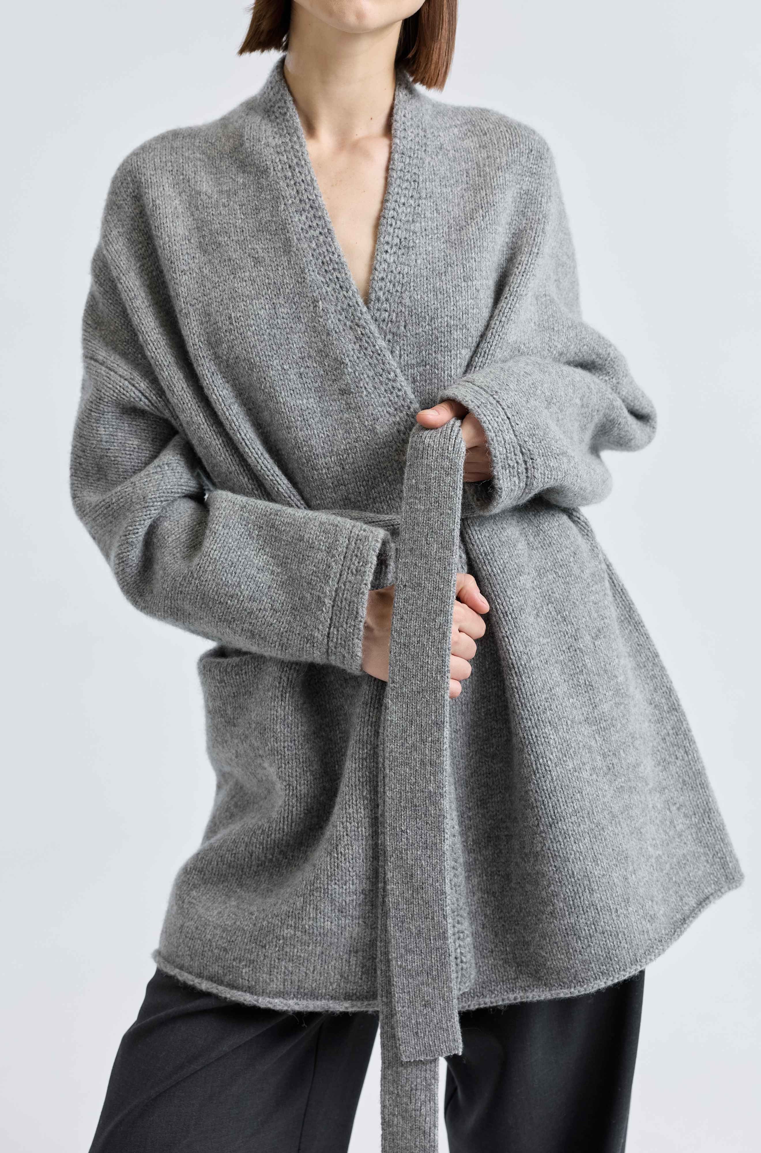 Person wearing a gray wrap-style sweater on a white background