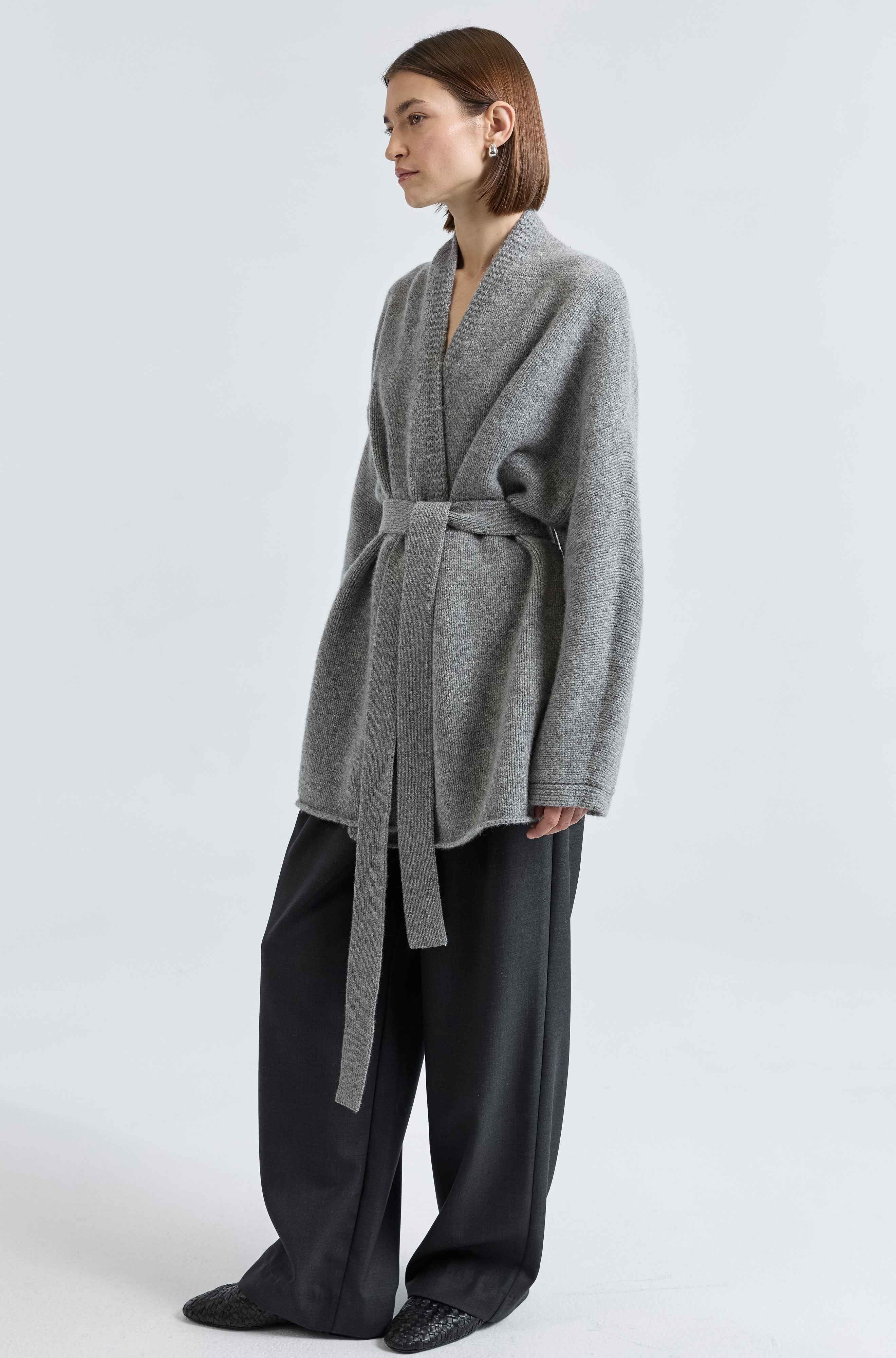 Person wearing a gray wool wrap sweater with a belt on a white background