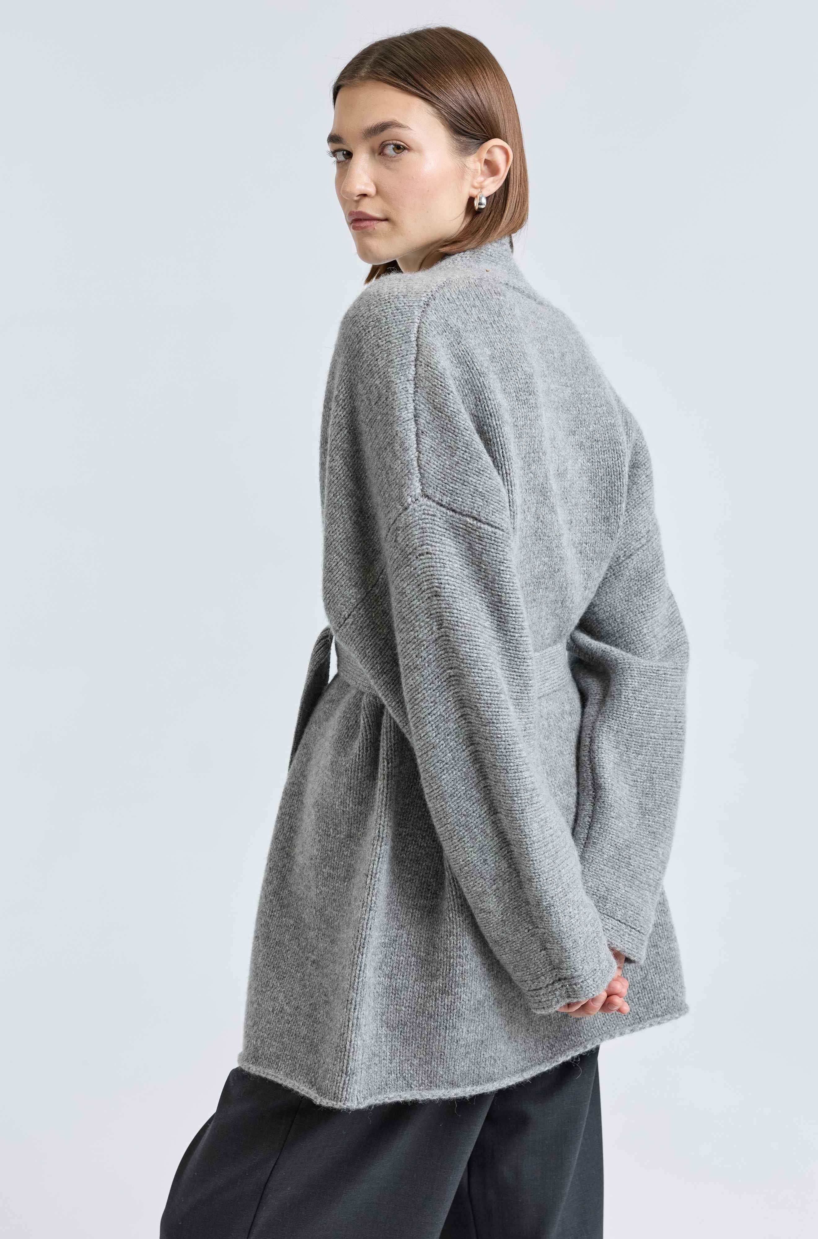 Person wearing a gray cardigan on a light gray background