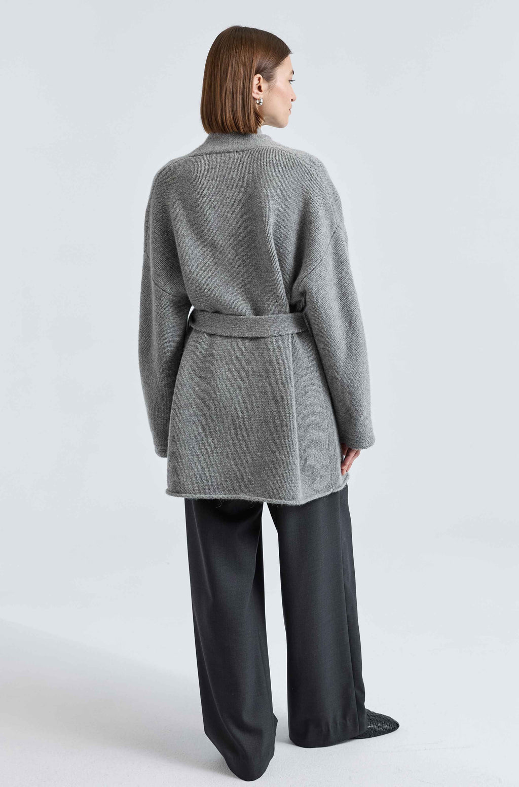 Person wearing a gray coat and black pants on a white background