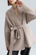 Woman wearing a beige wool wrap sweater on a light grey background
