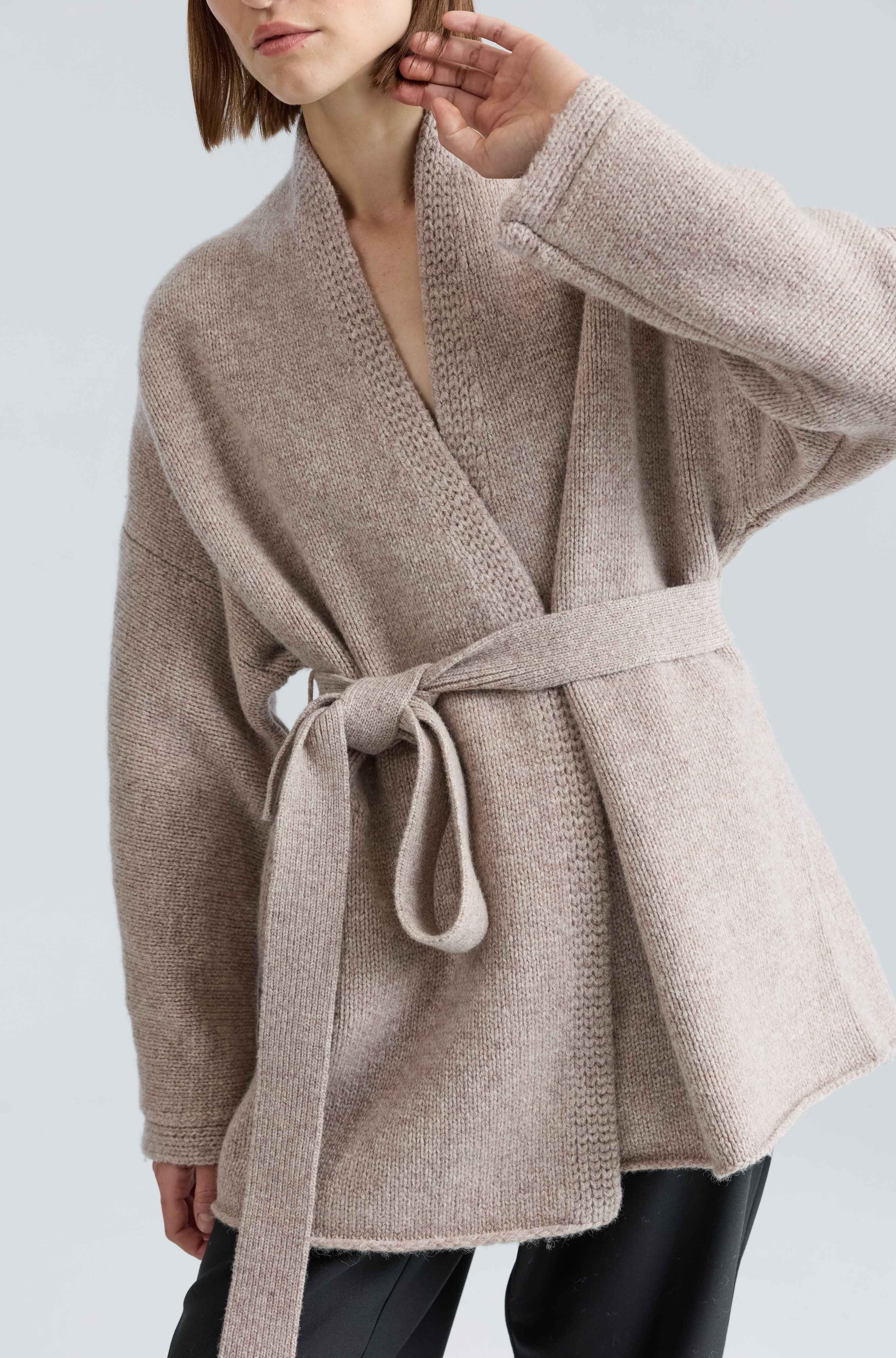 Woman wearing a beige wool wrap sweater on a light grey background
