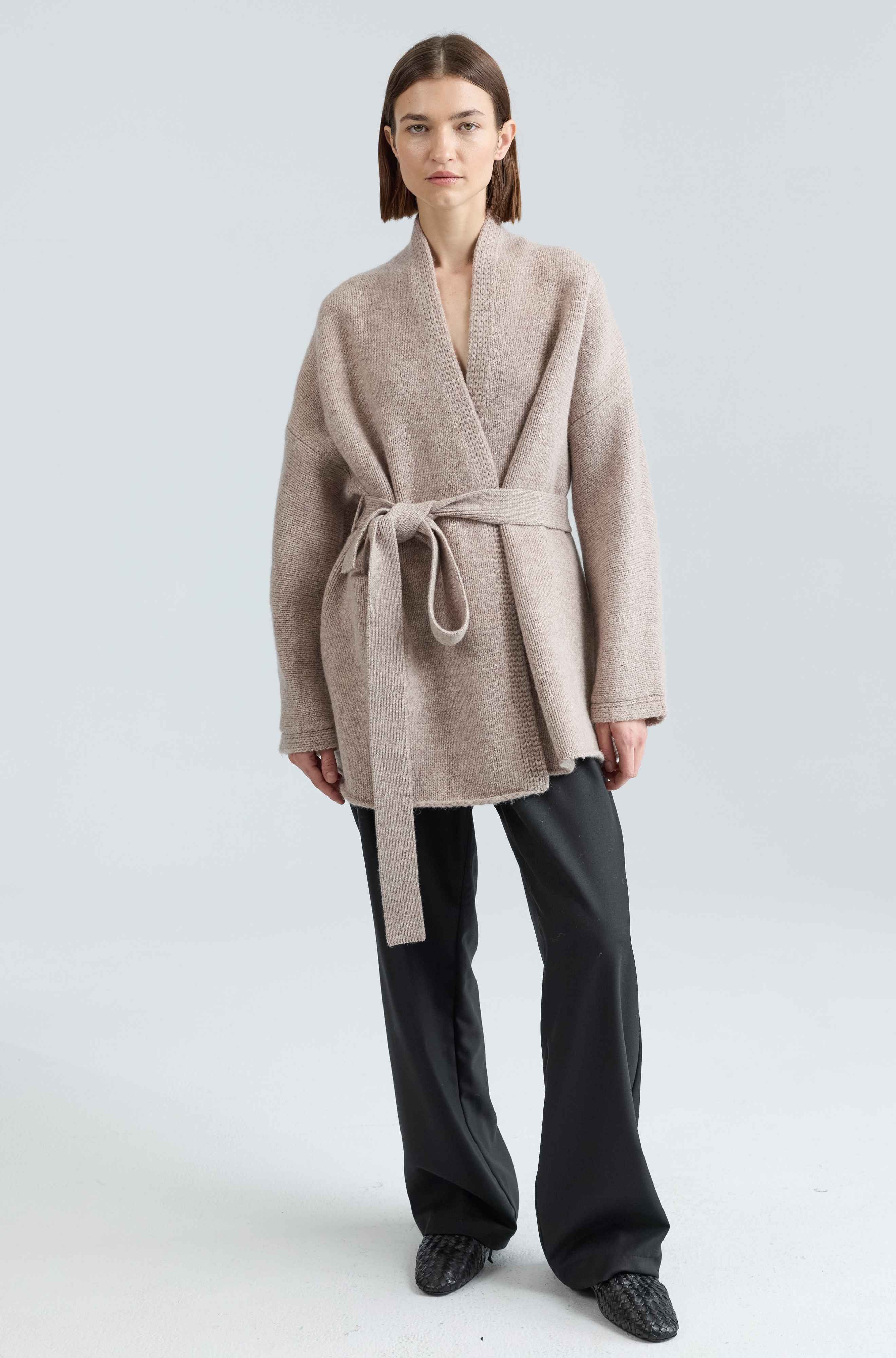 Woman wearing a beige belted coat on a light gray background
