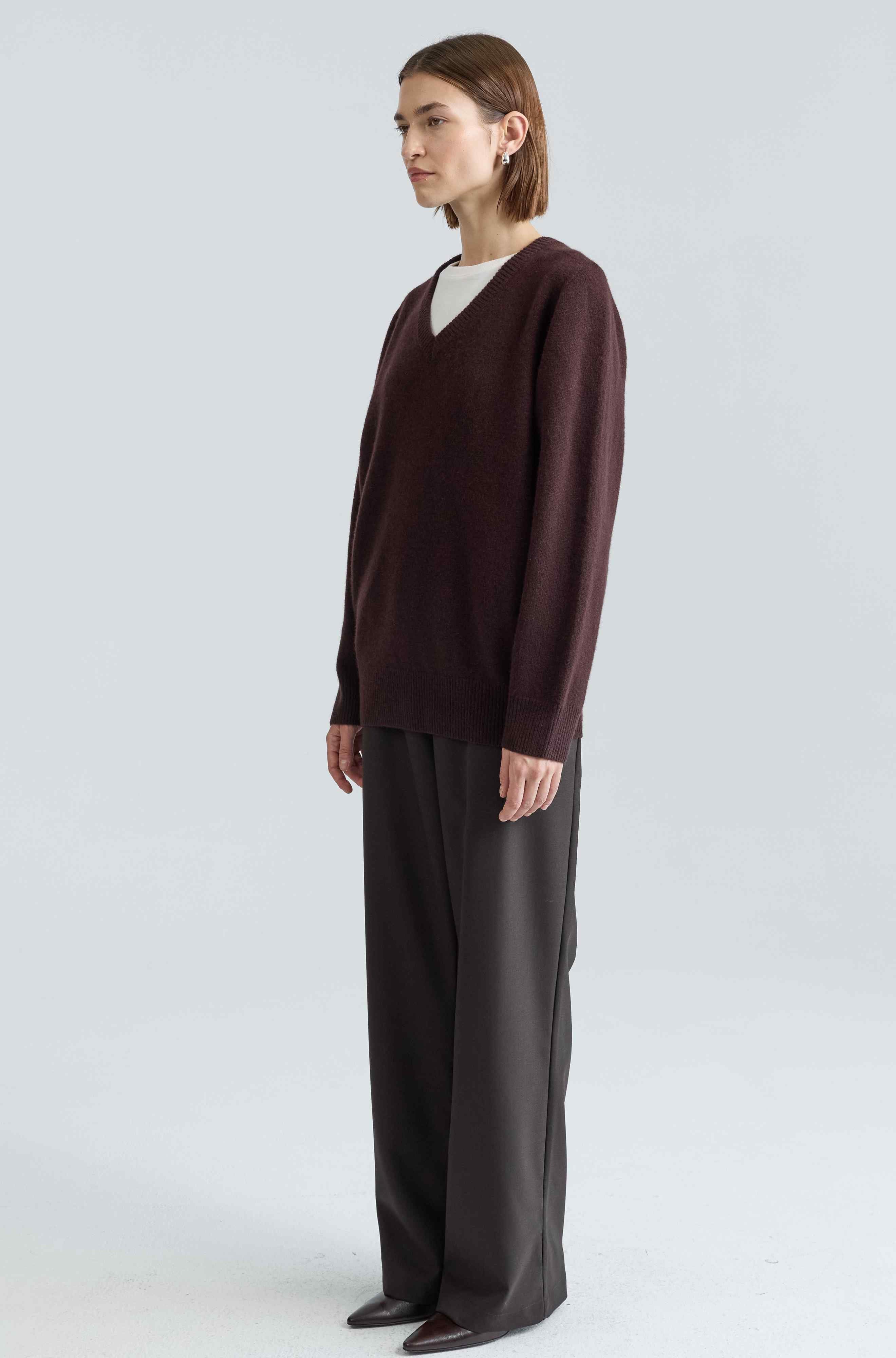 Person wearing a brown sweater and dark pants on a white background