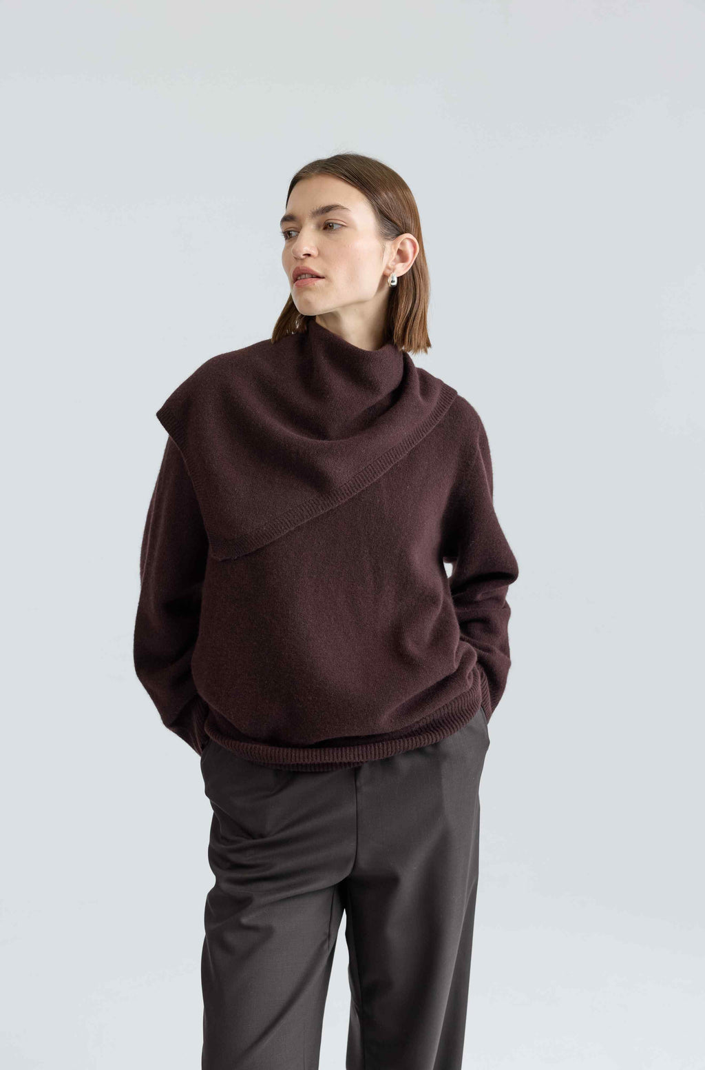 Person wearing a brown sweater and dark pants on a light gray background