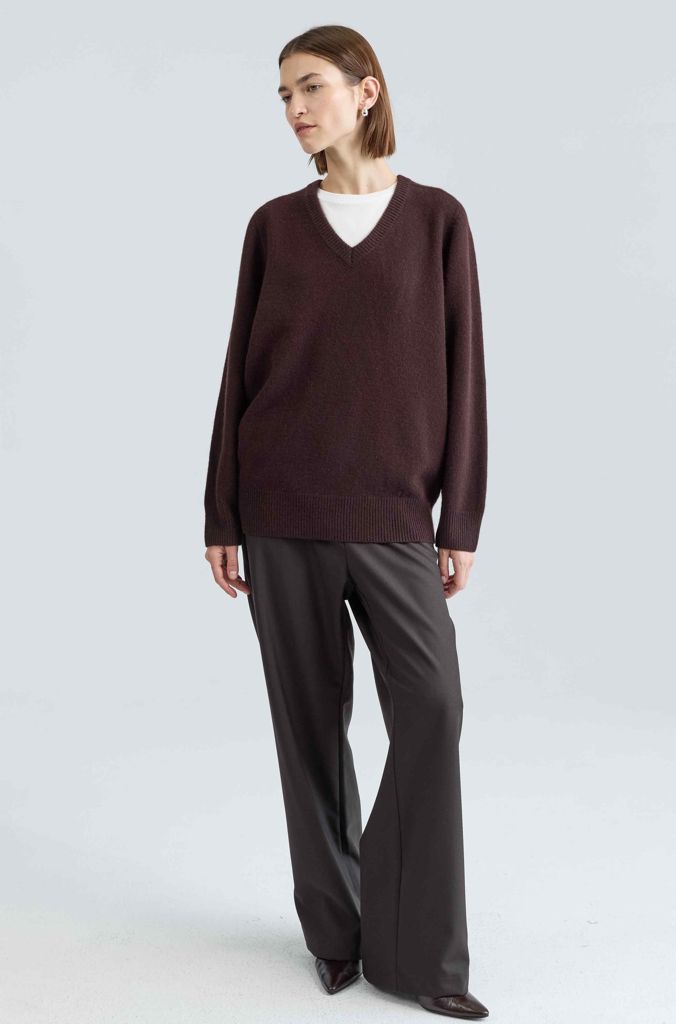 Woman wearing a brown sweater and gray pants on a light gray background