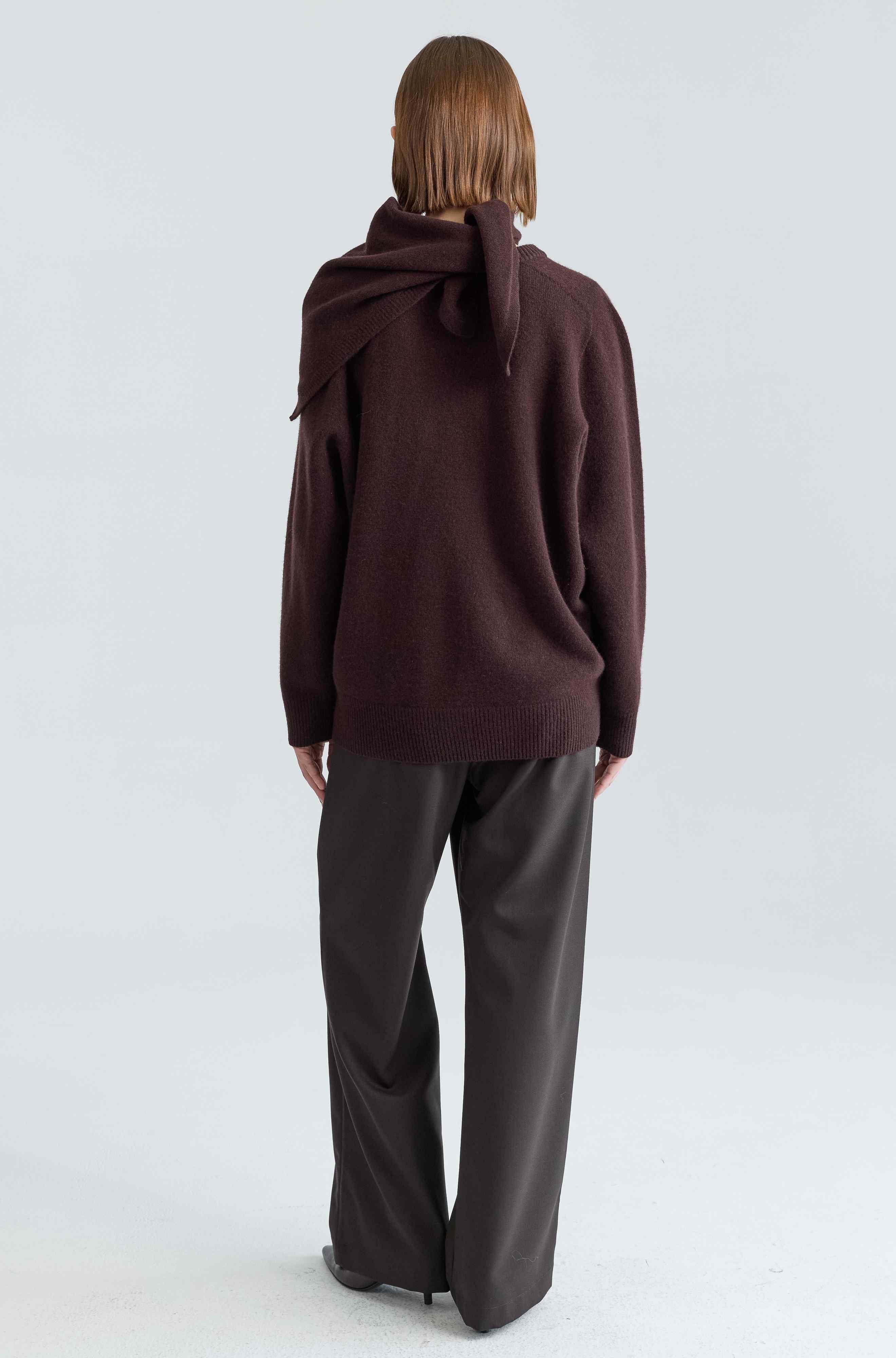 Person wearing a brown wool sweater and dark pants on a white background