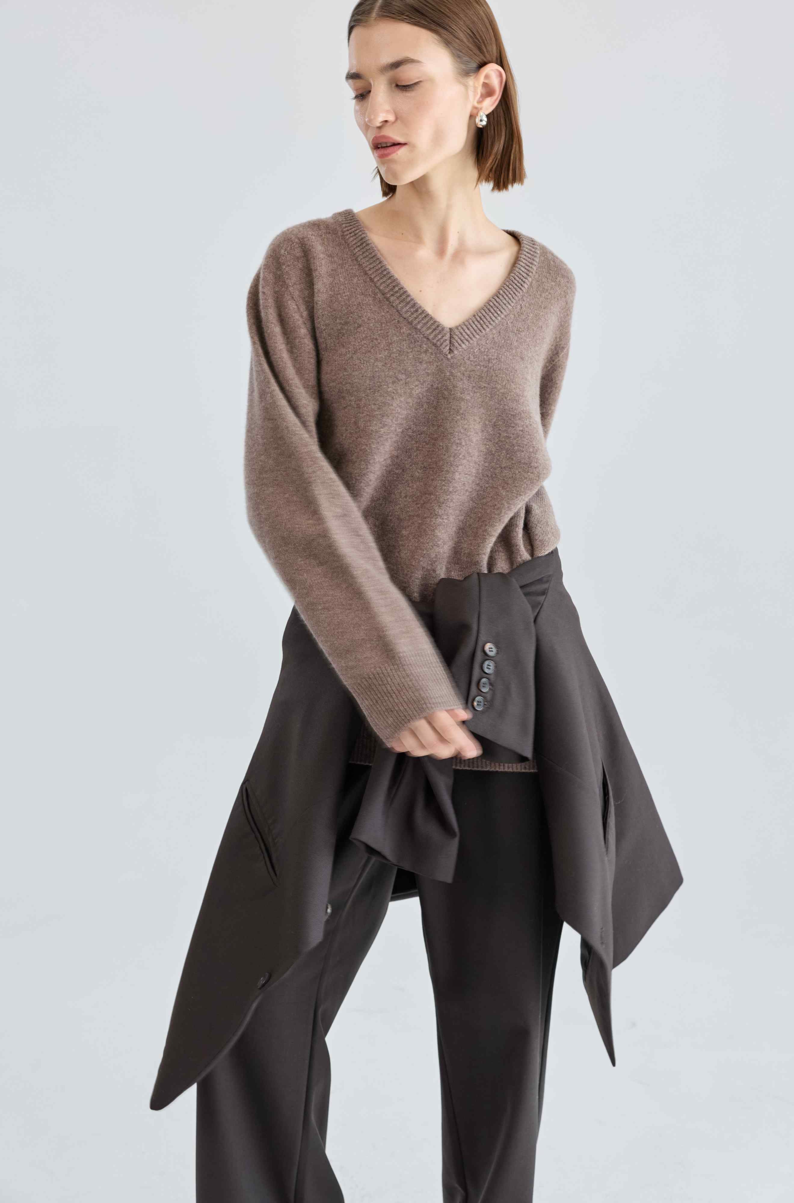 Woman wearing a brown sweater and dark pants on a light gray background