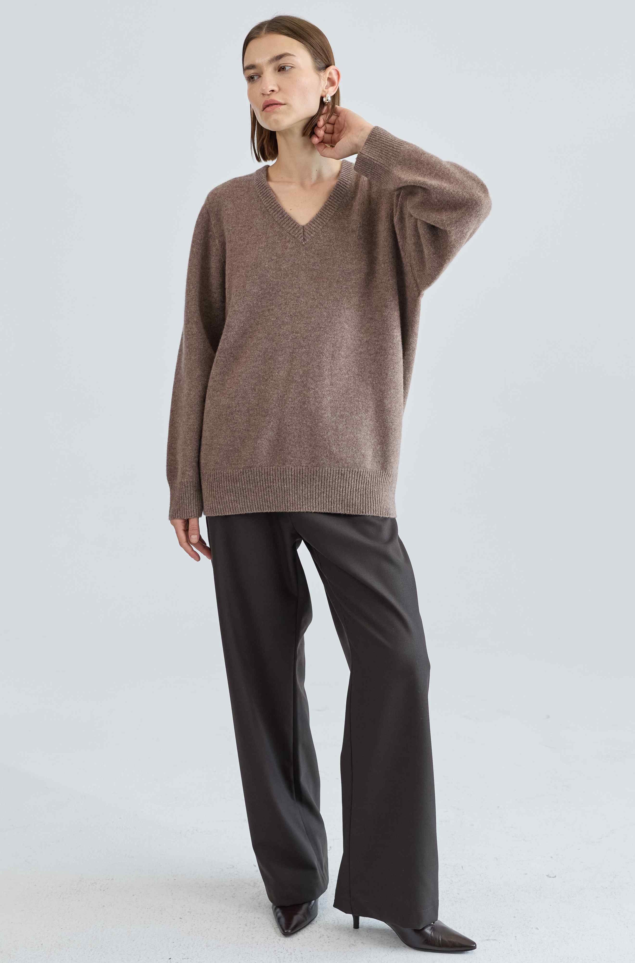 Woman wearing a brown sweater and black pants on a light gray background