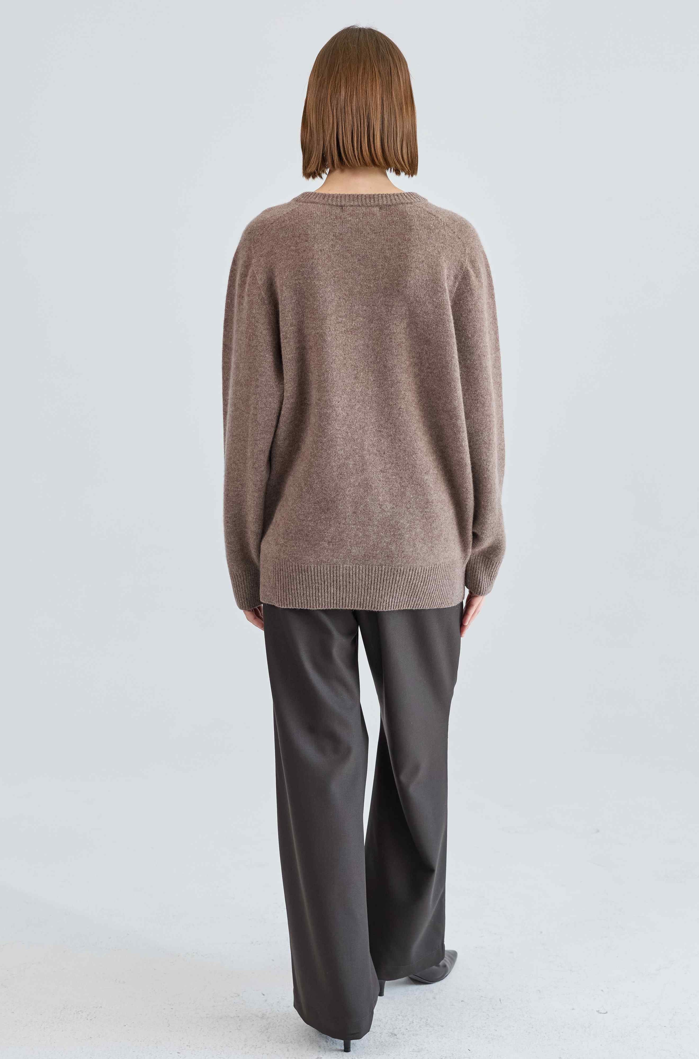 Person wearing a brown sweater and dark pants on a light gray background