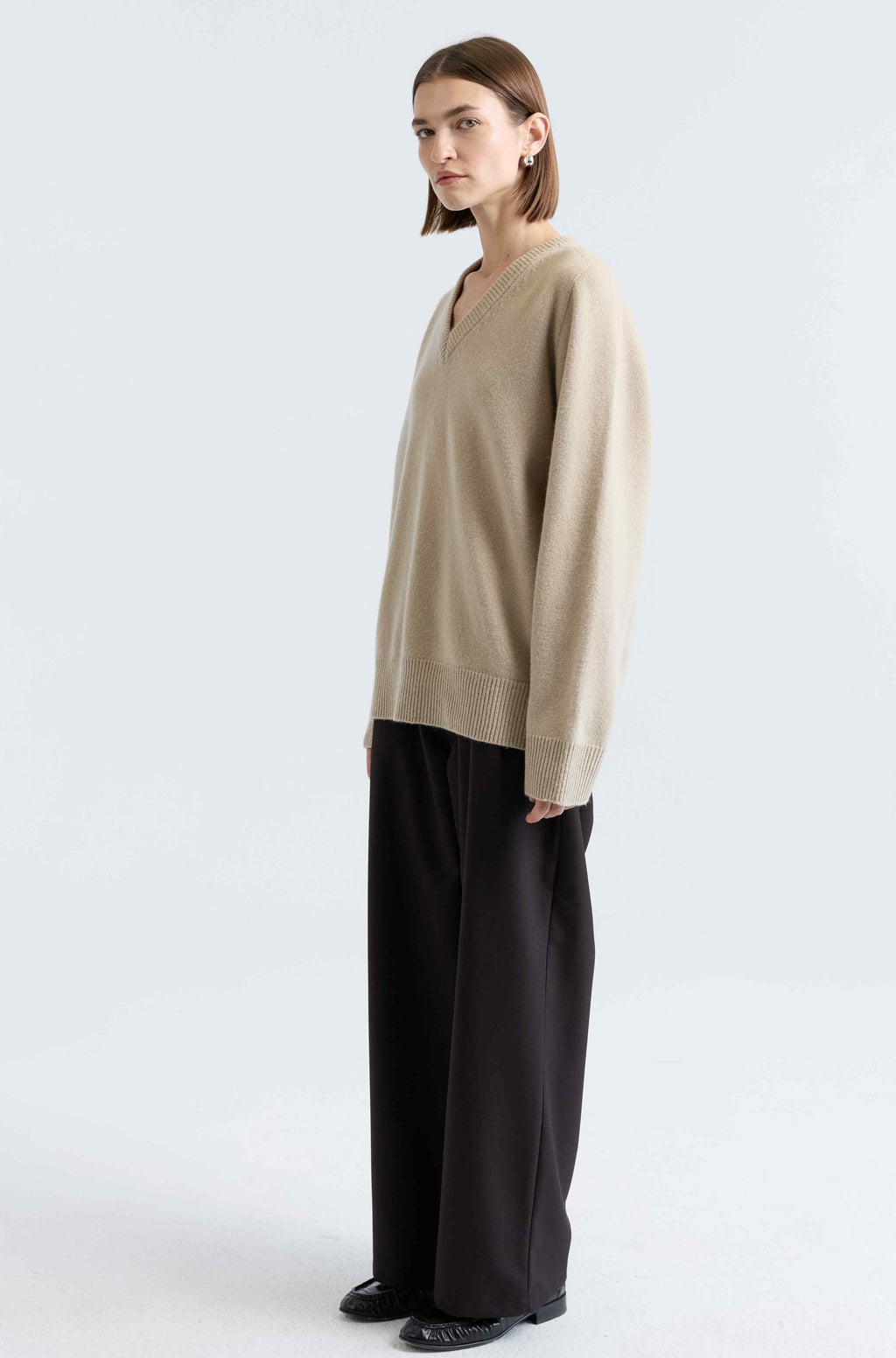 Woman wearing a beige sweater and dark pants on a white background
