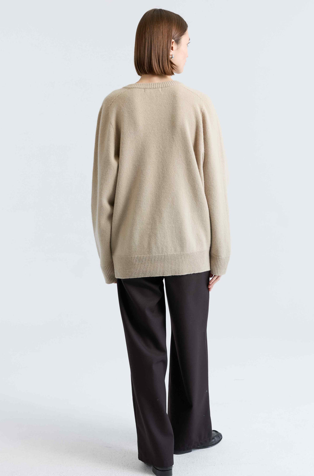 Person wearing a beige sweater and dark pants on a white background