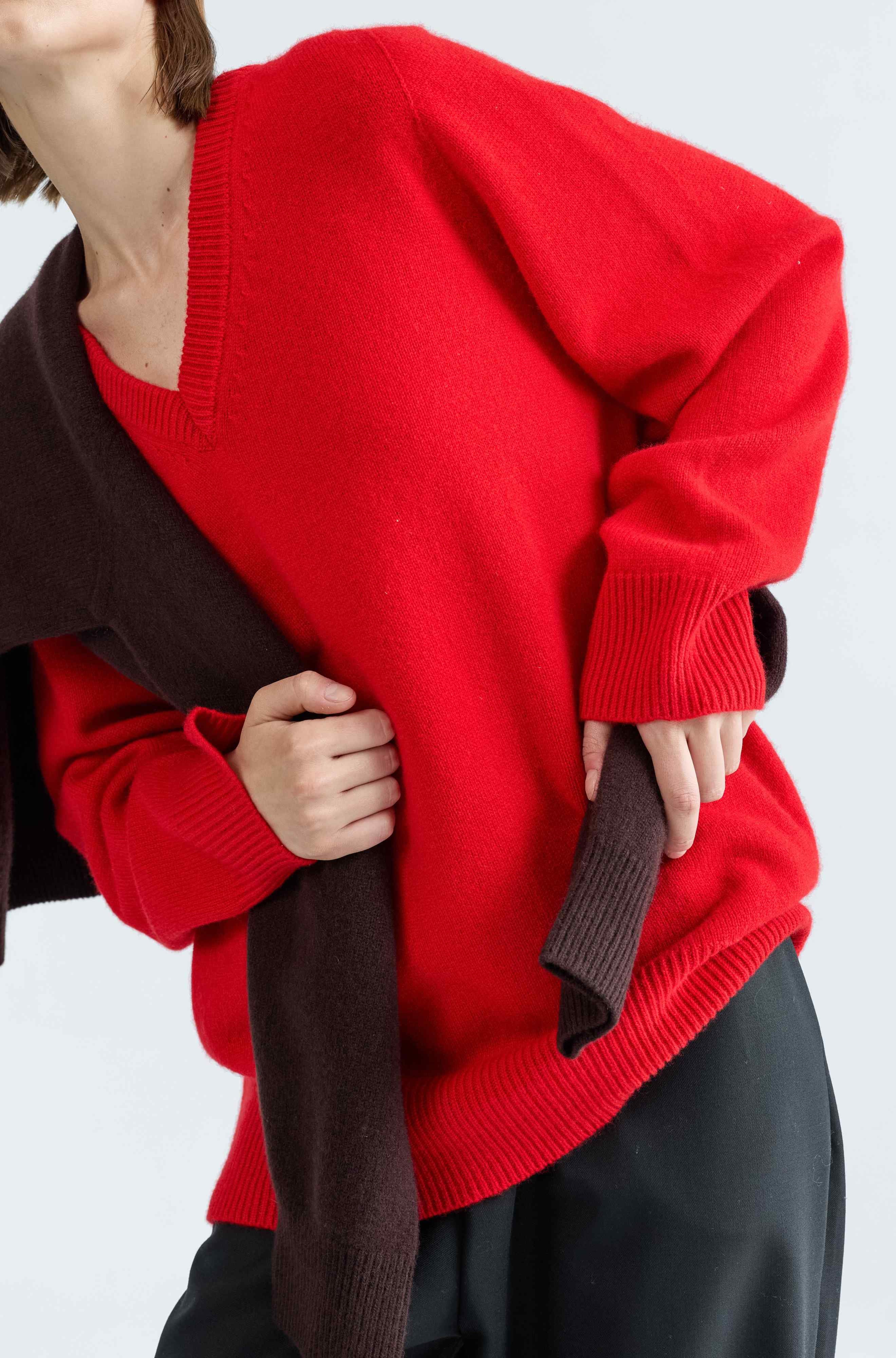 Person wearing a red sweater over a dark coat on a white background
