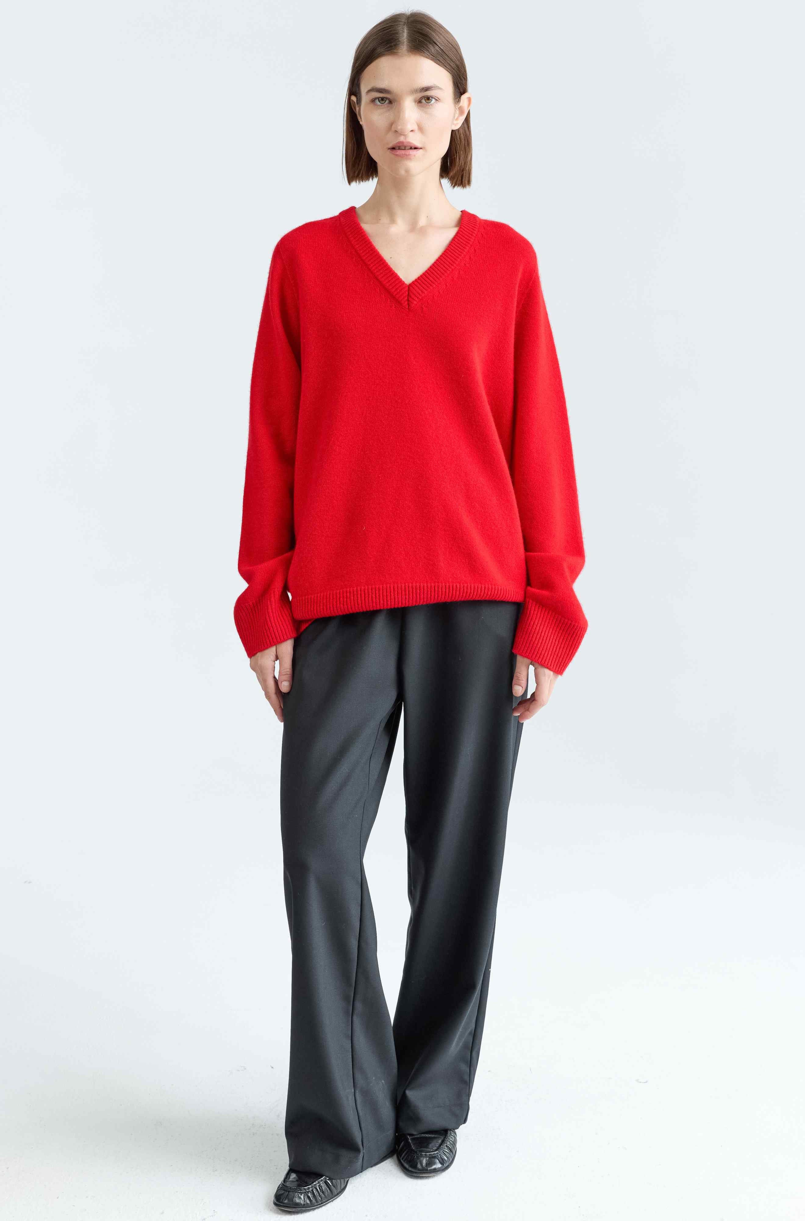 Person wearing a red sweater and black pants on a white background
