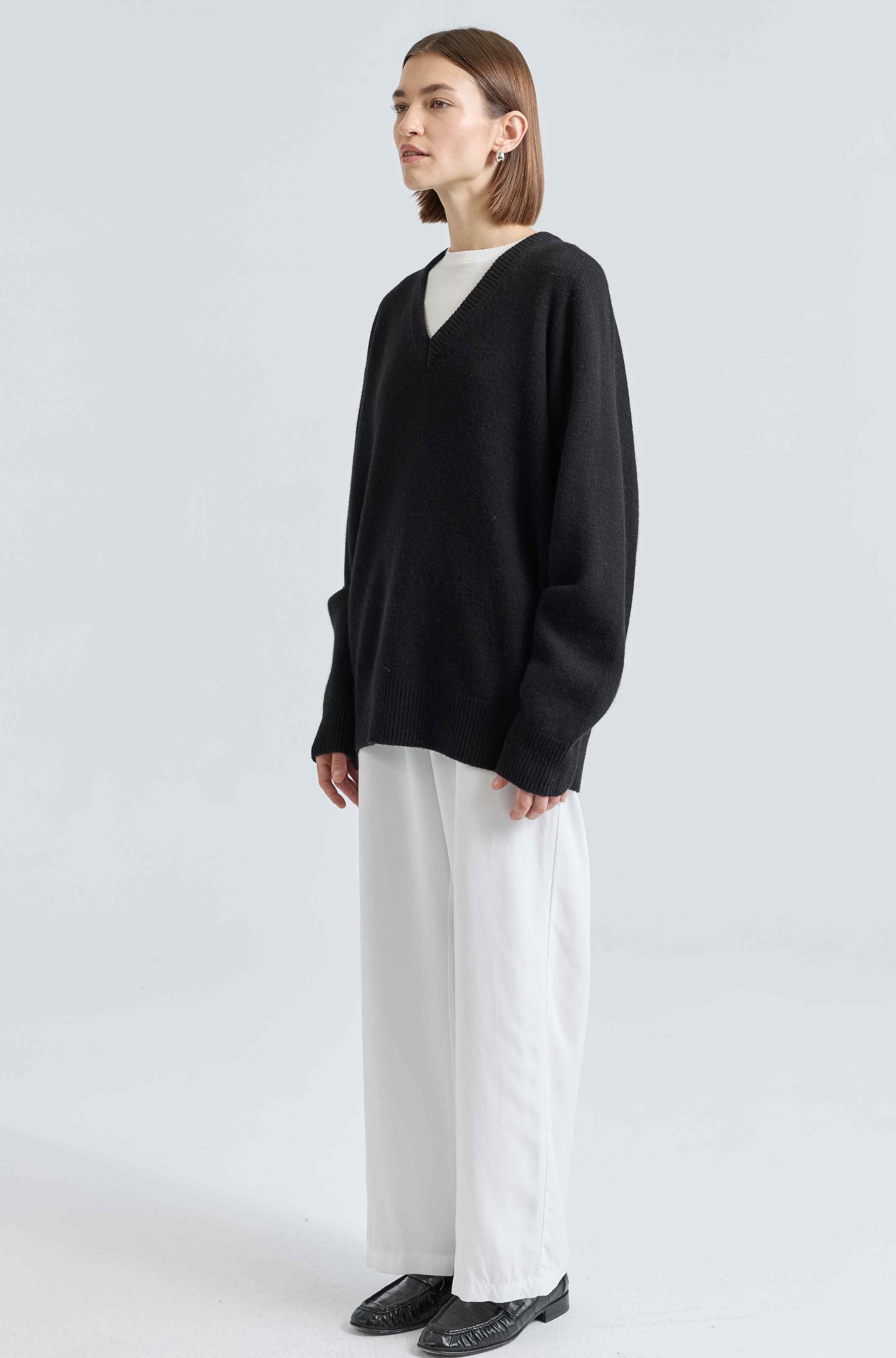 Person wearing a black sweater and white pants on a light gray background