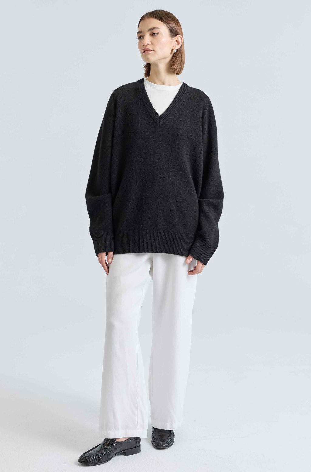 Person wearing a black sweater and white pants on a light gray background