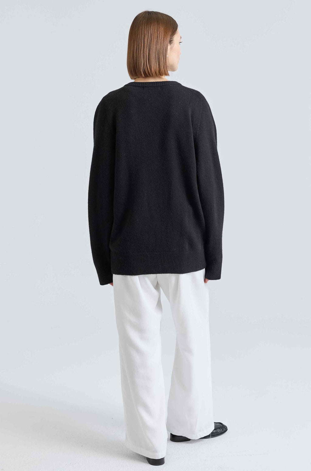 Person wearing a black sweater and white pants on a light gray background