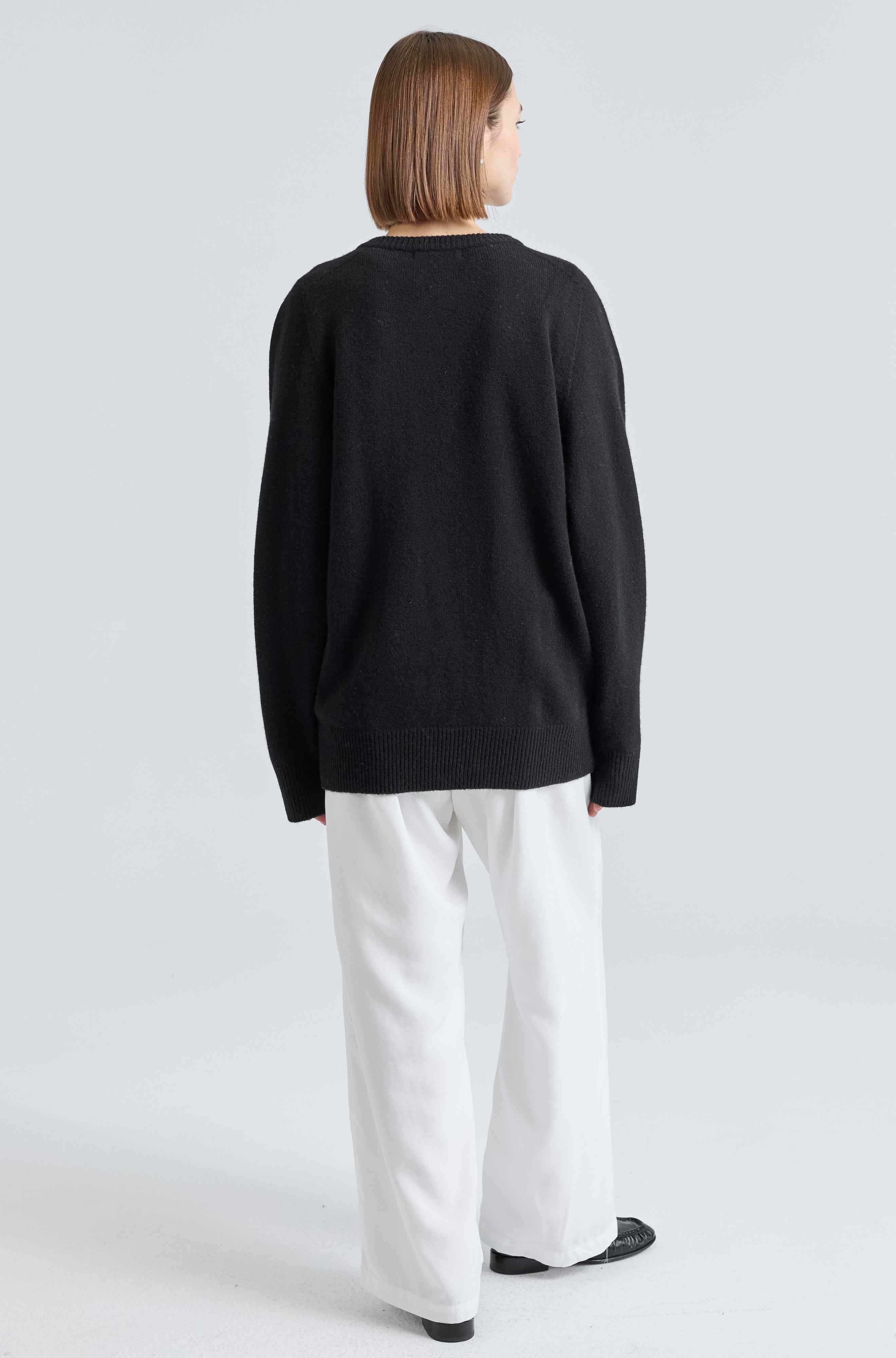 Person wearing a black sweater and white pants on a light gray background