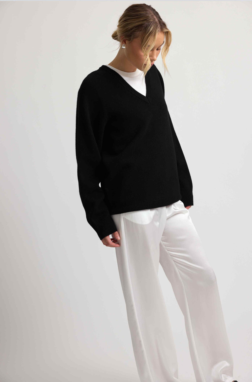 Person wearing a black sweater and white pants on a plain background