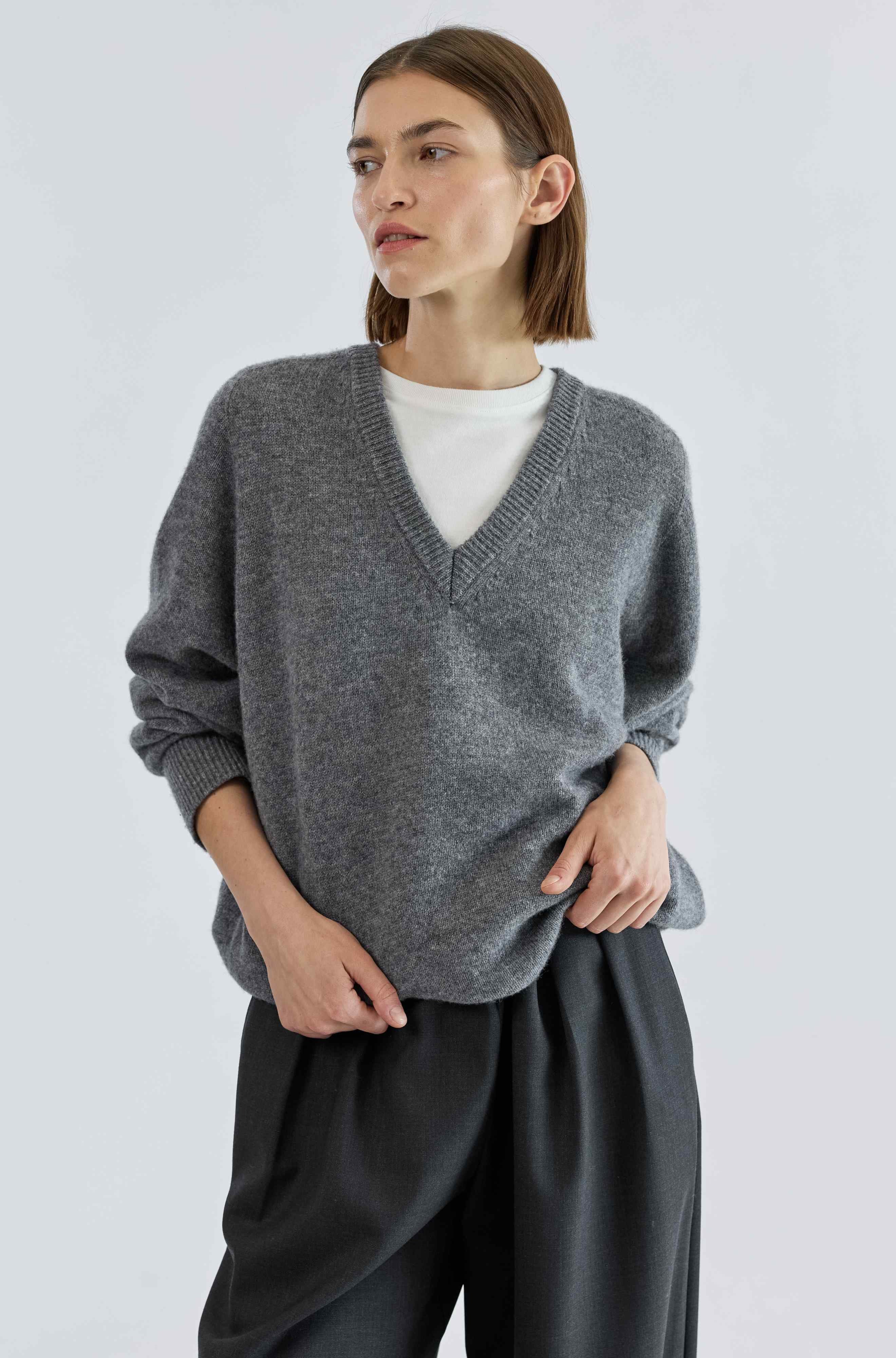 Woman wearing a gray sweater and black pants on a white background