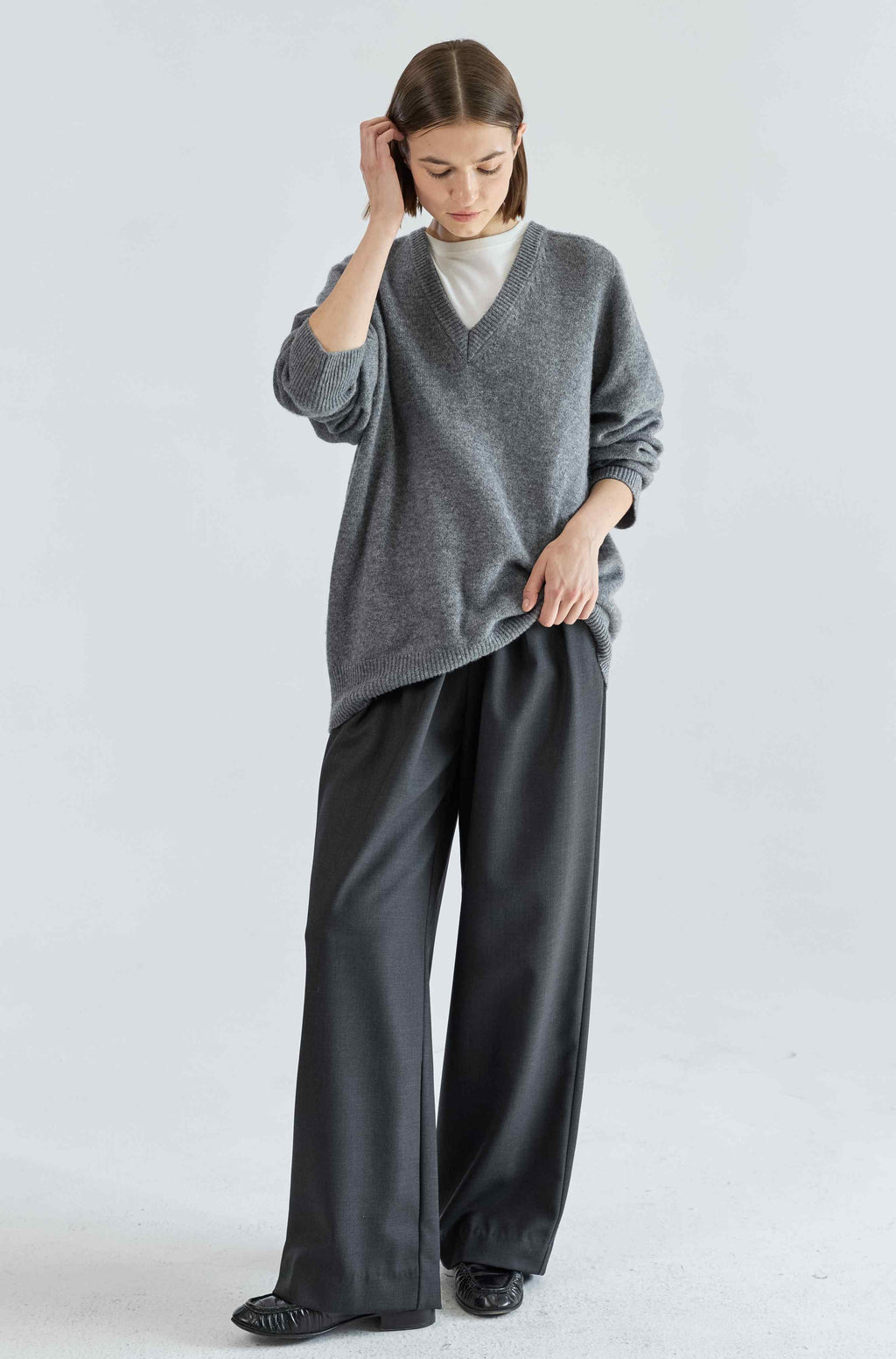 Woman wearing a gray sweater and black pants on a white background