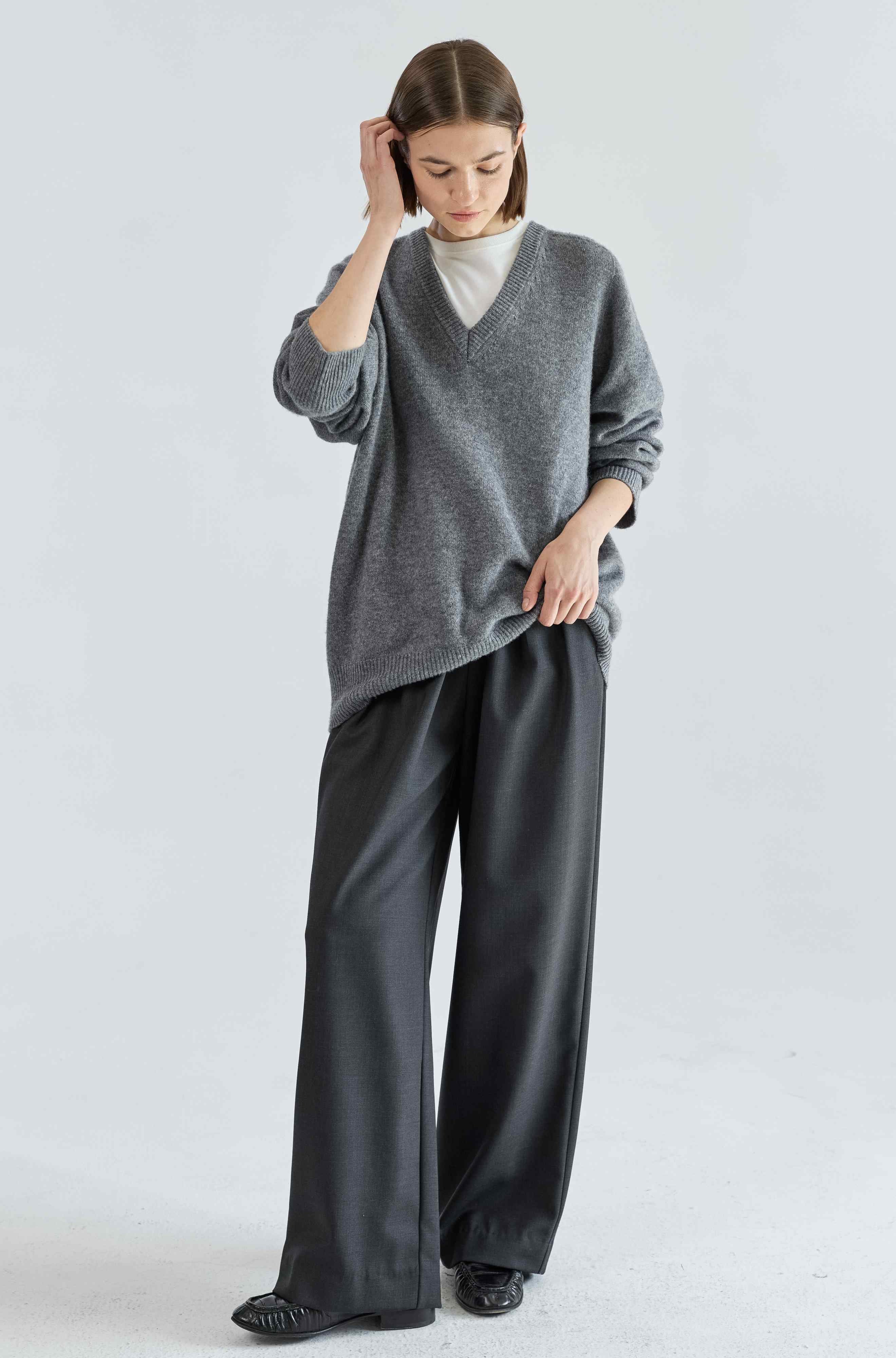 Woman wearing a gray sweater and black pants on a white background