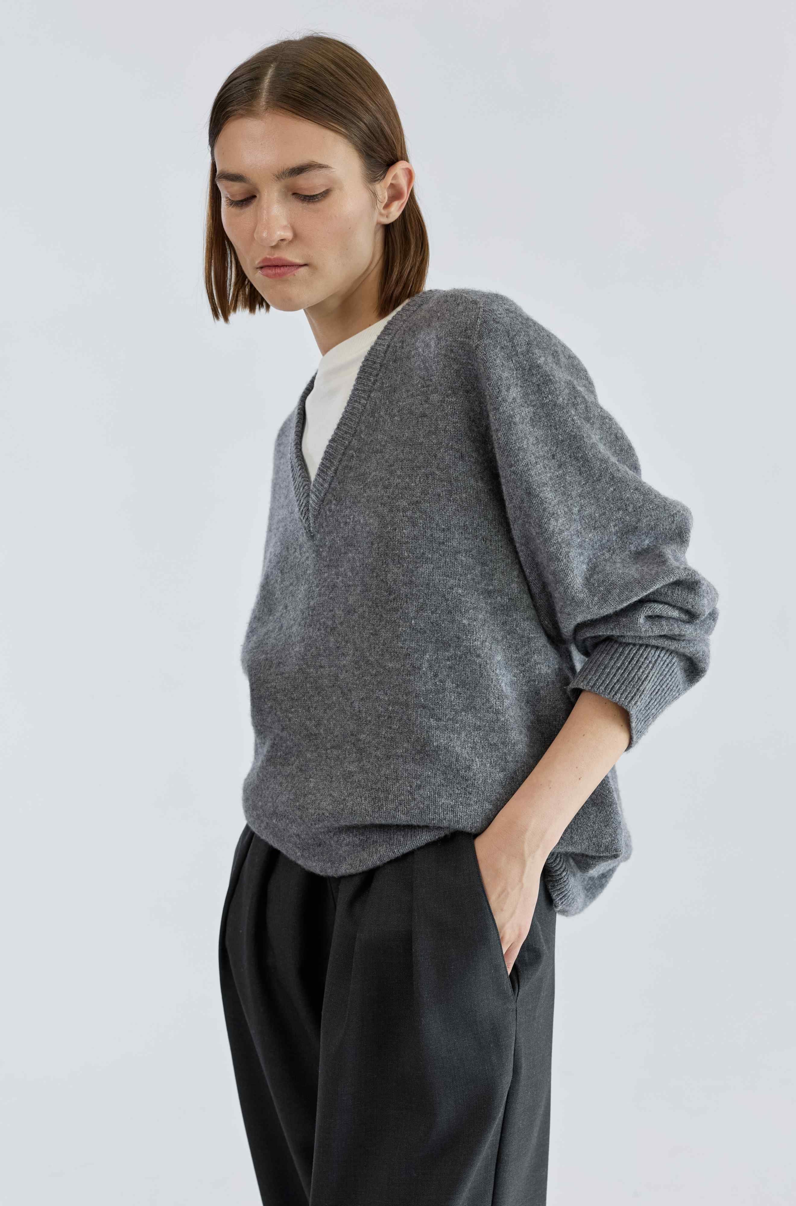 Woman wearing a grey wool v neck sweater against a light grey background