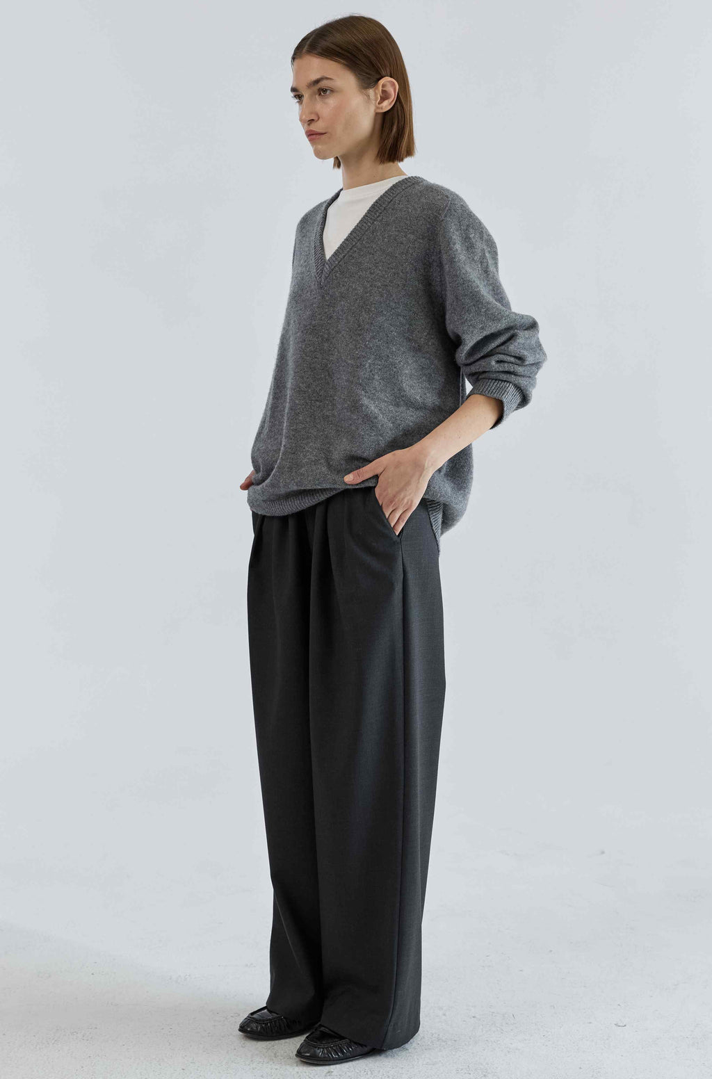 Person wearing a gray sweater and black pants on a white background