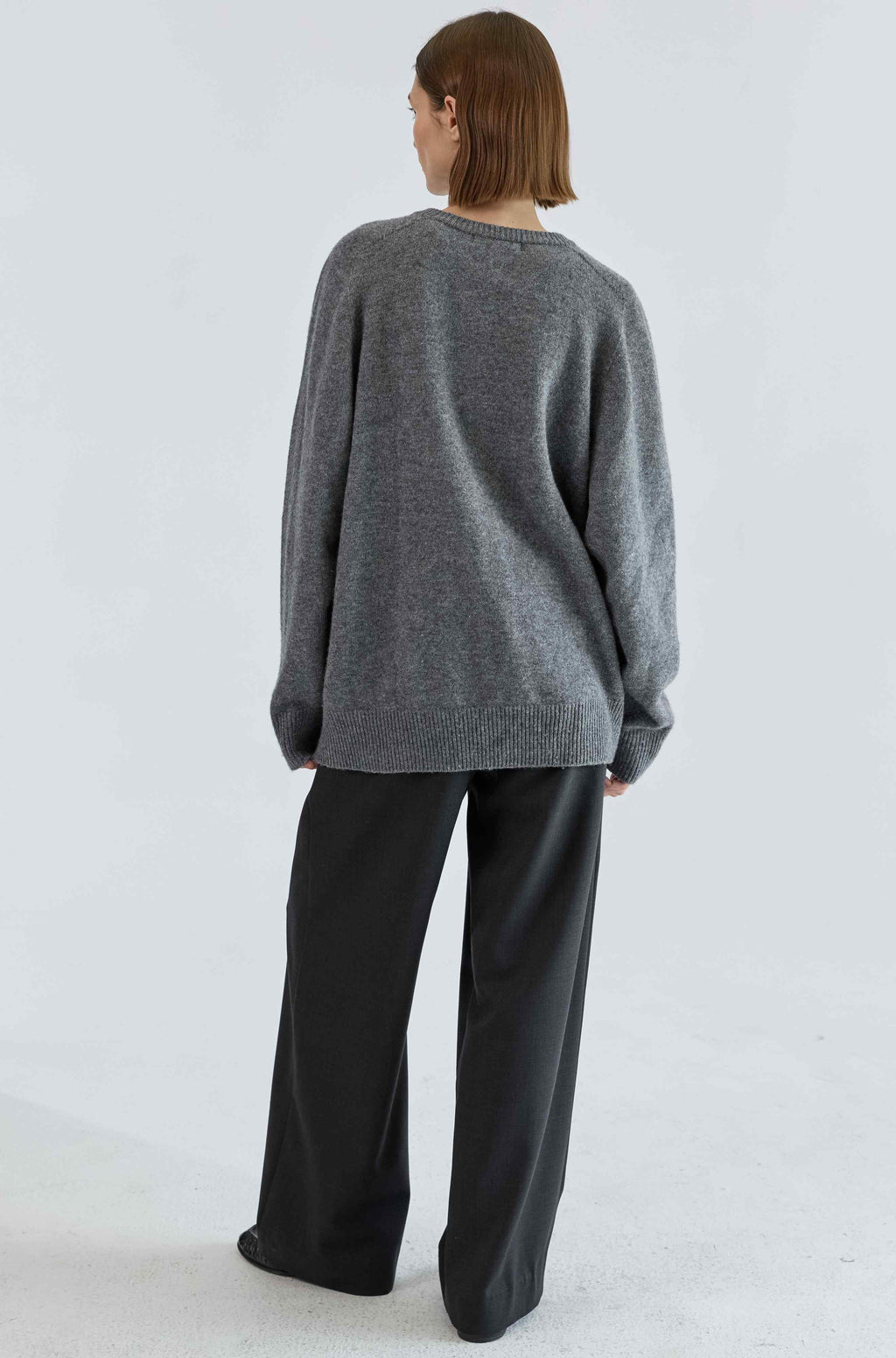 Person wearing a gray sweater and black pants on a light gray background