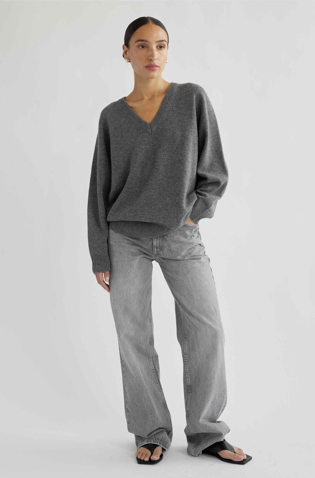 Person wearing a gray sweater and jeans on a white background