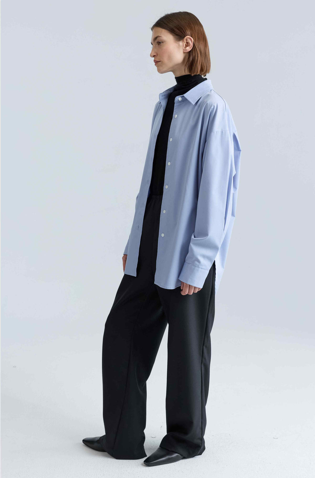 Person wearing a light blue shirt over a black top with black pants on a white background