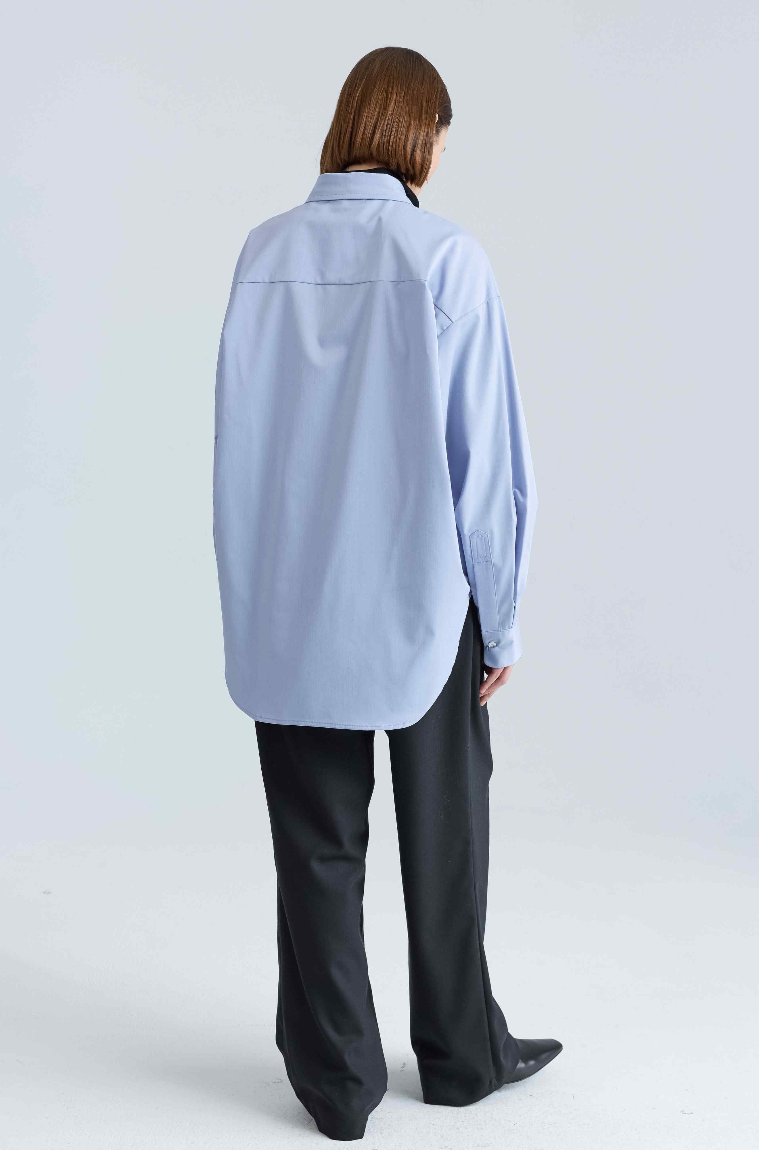 Person wearing a light blue shirt and black pants on a white background