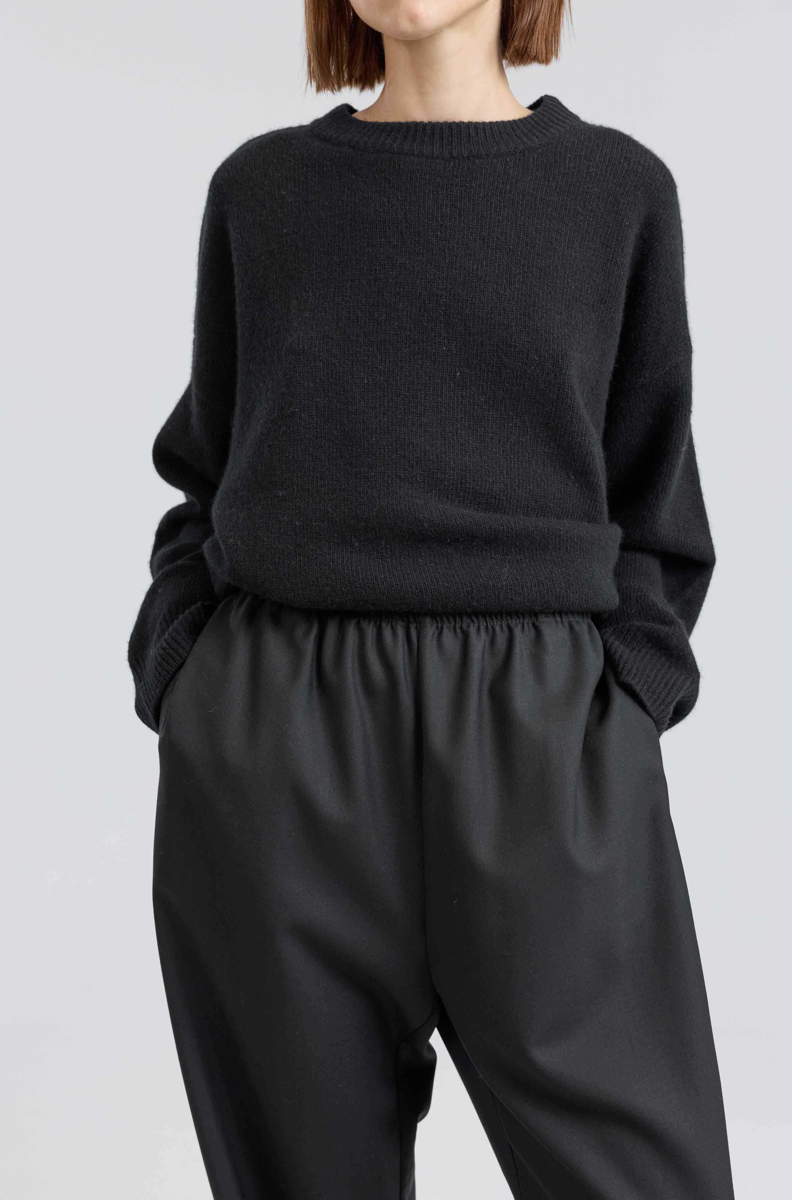 Person wearing a black sweater and black pants on a white background