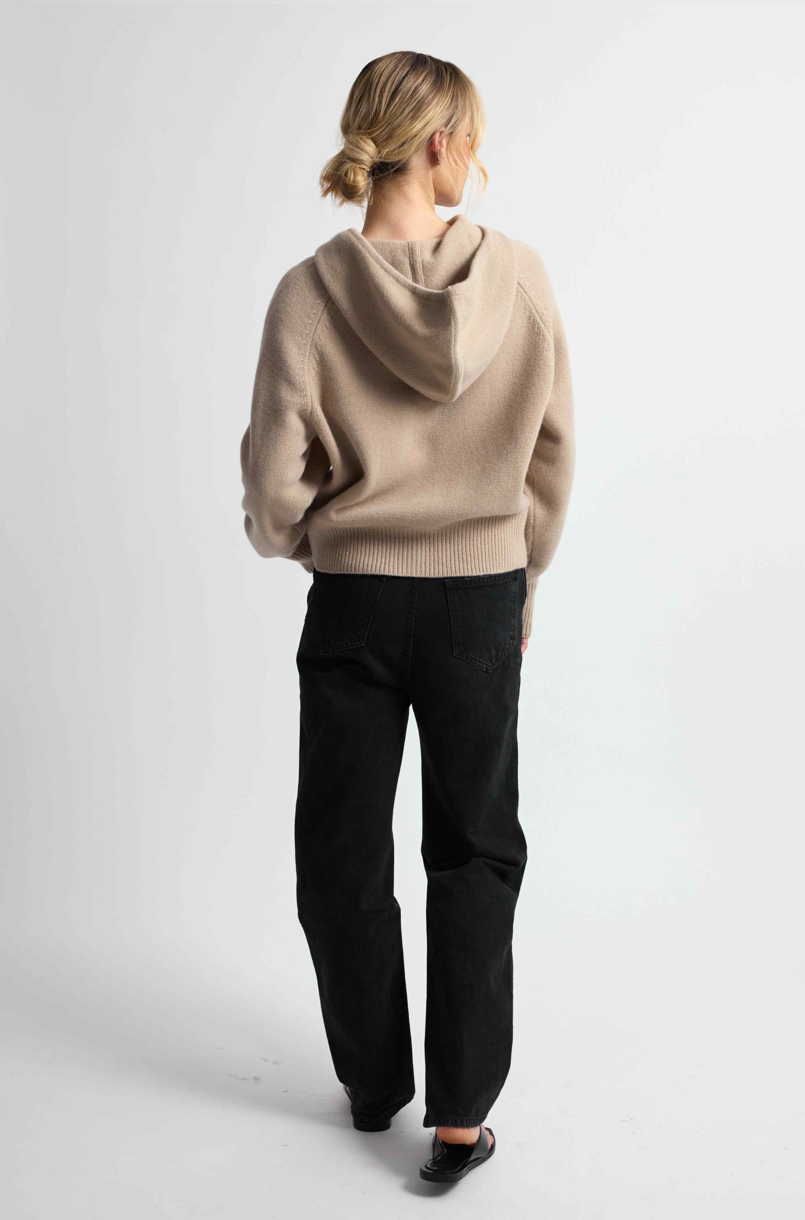 Person wearing a beige hoodie and black pants on a white background