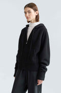 Person wearing a black hoodie and pants on a light gray background